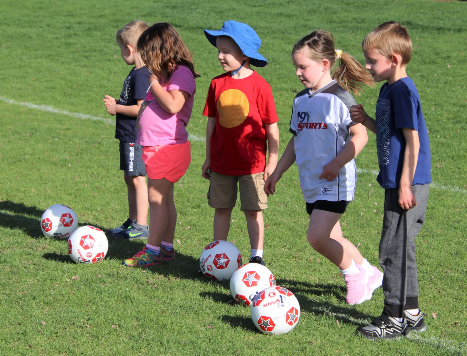 a group of kids stand around some football balls