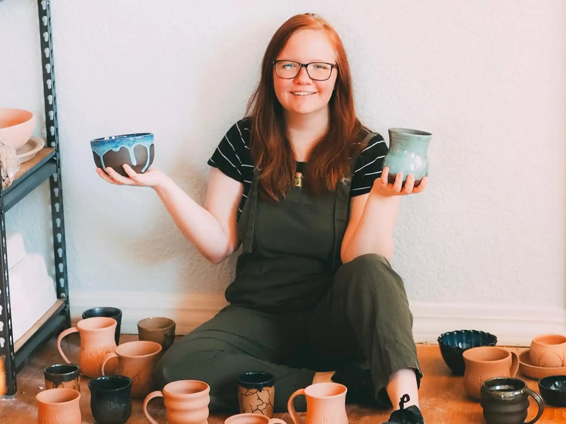 a woman sitting on a table with a group of small pots and cups