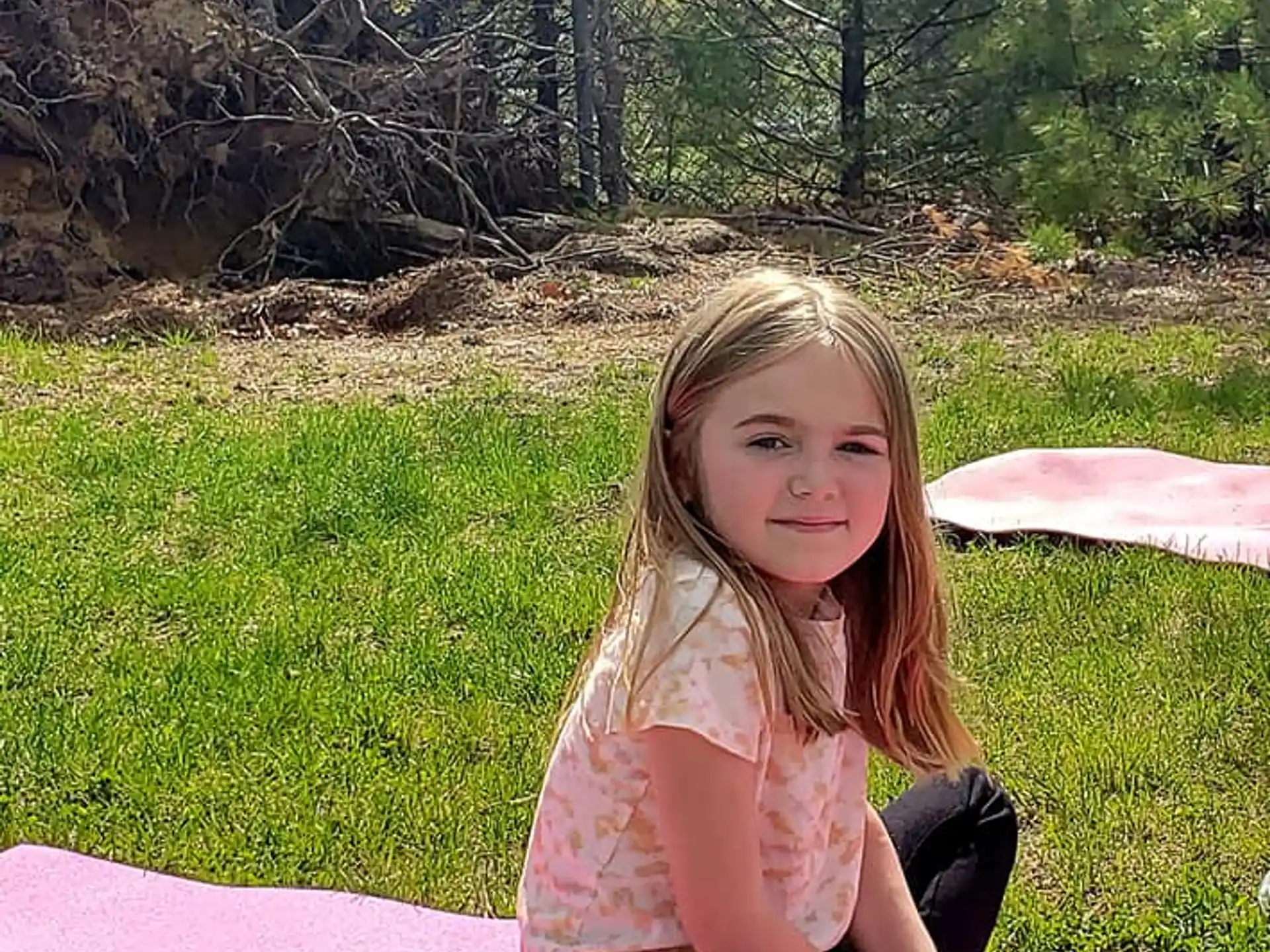 a girl sitting on a blanket in a grassy area with trees in the background