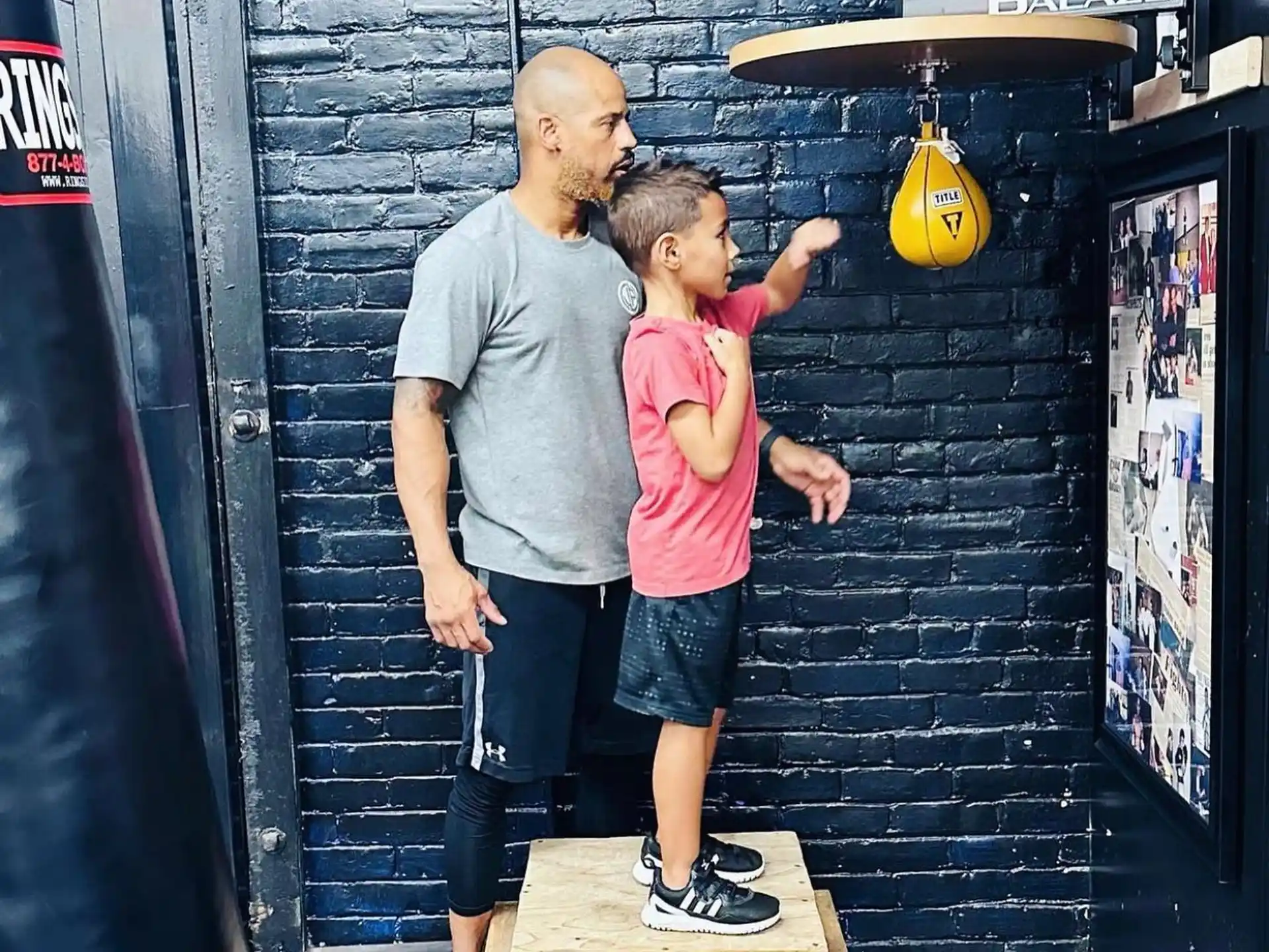 a person and a boy standing on a wood platform in front of a brick wall with a wood