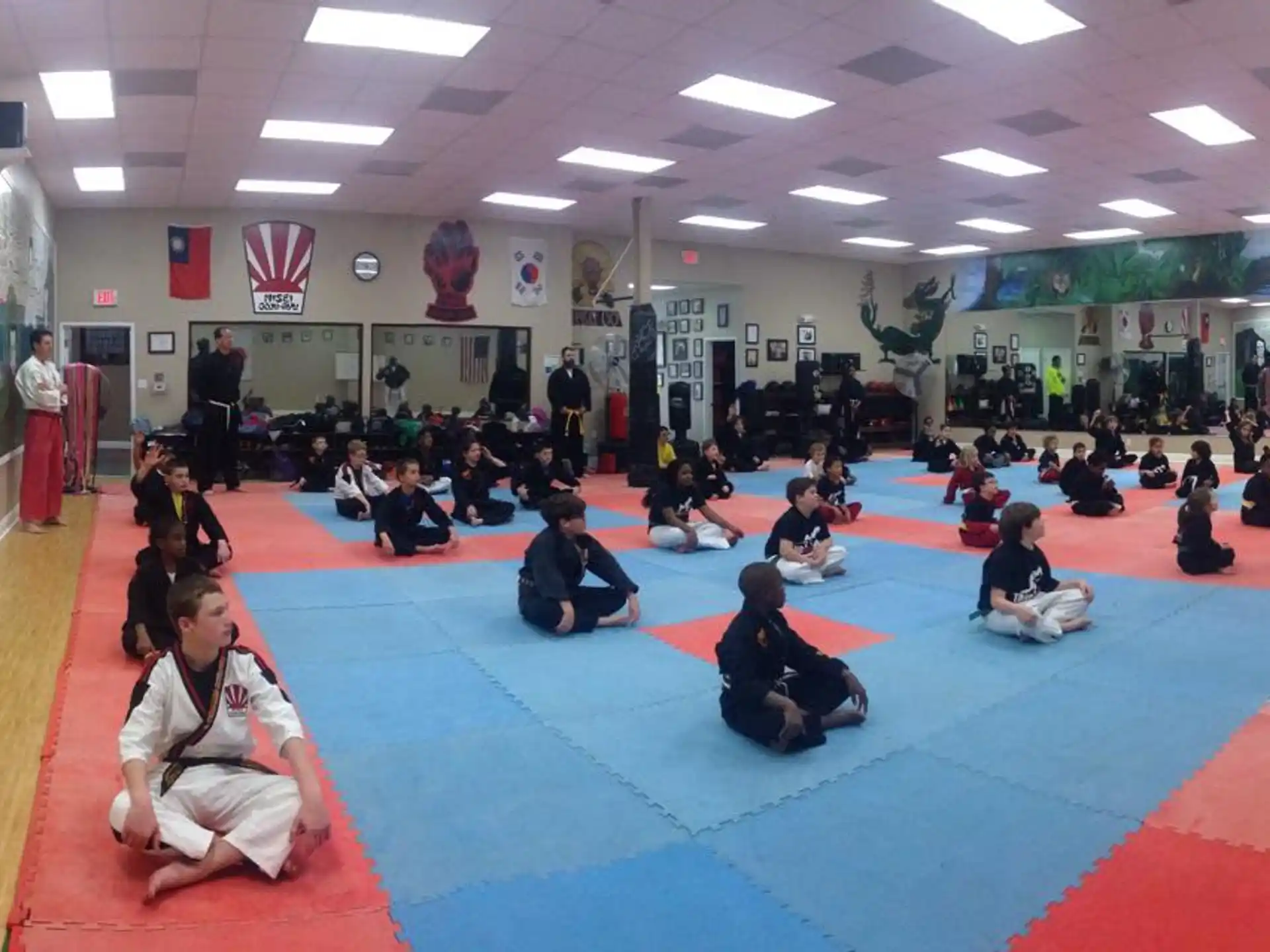 a group of people sitting on a mat in a room with flags