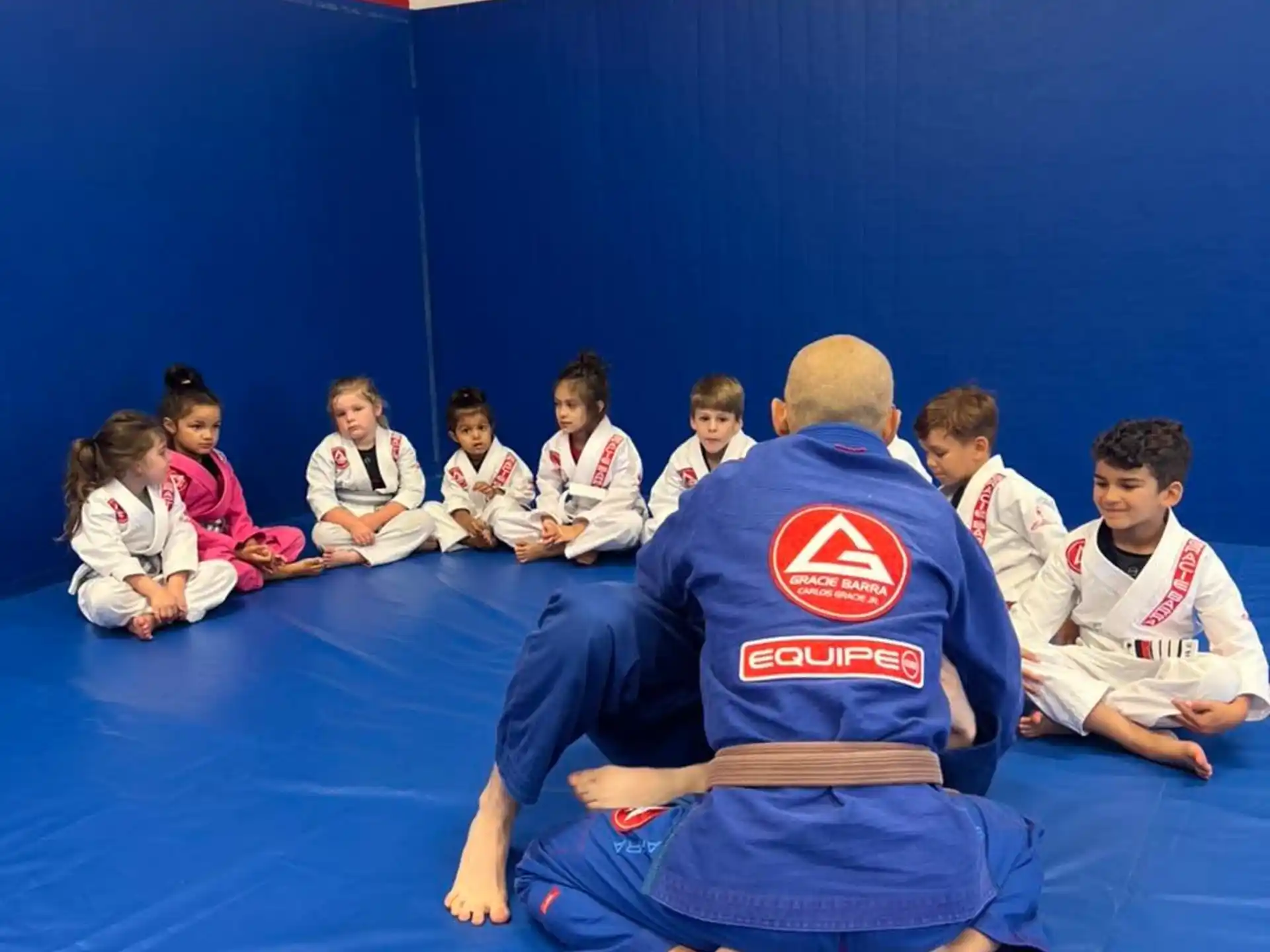a person in a blue uniform kneeling on the floor with a group of people in the back