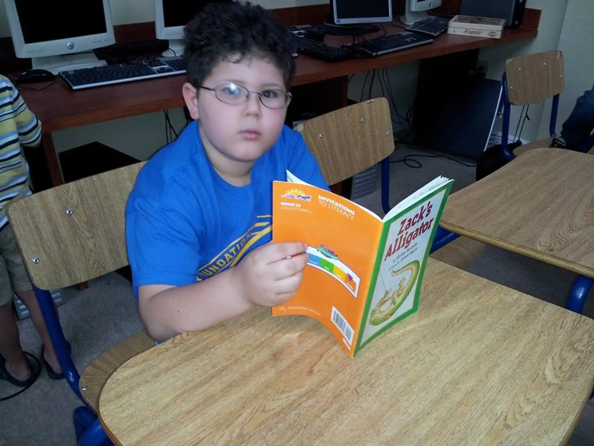 a boy sitting at a desk reading a book