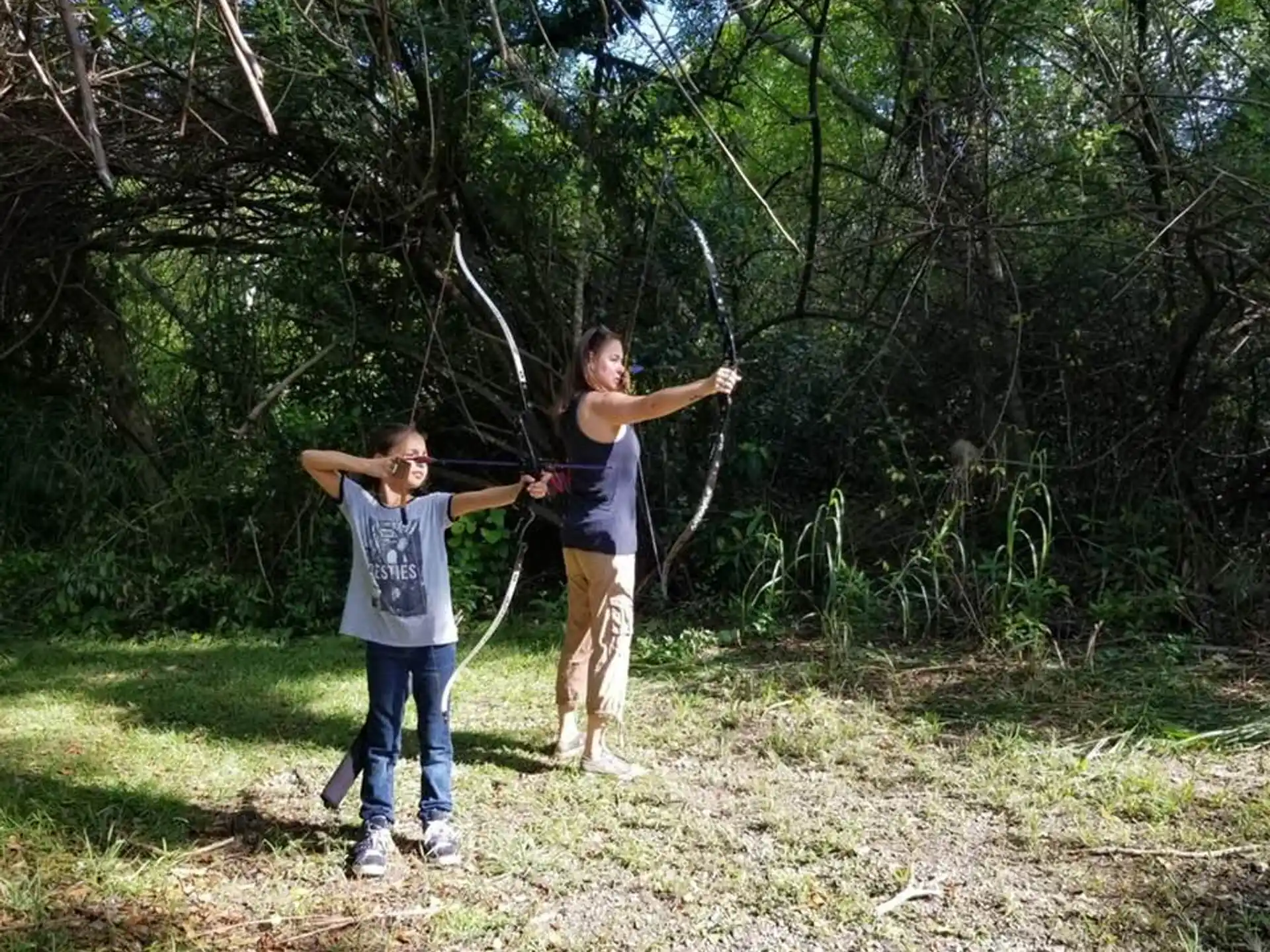 a person and a boy holding a bow and arrow in a forest