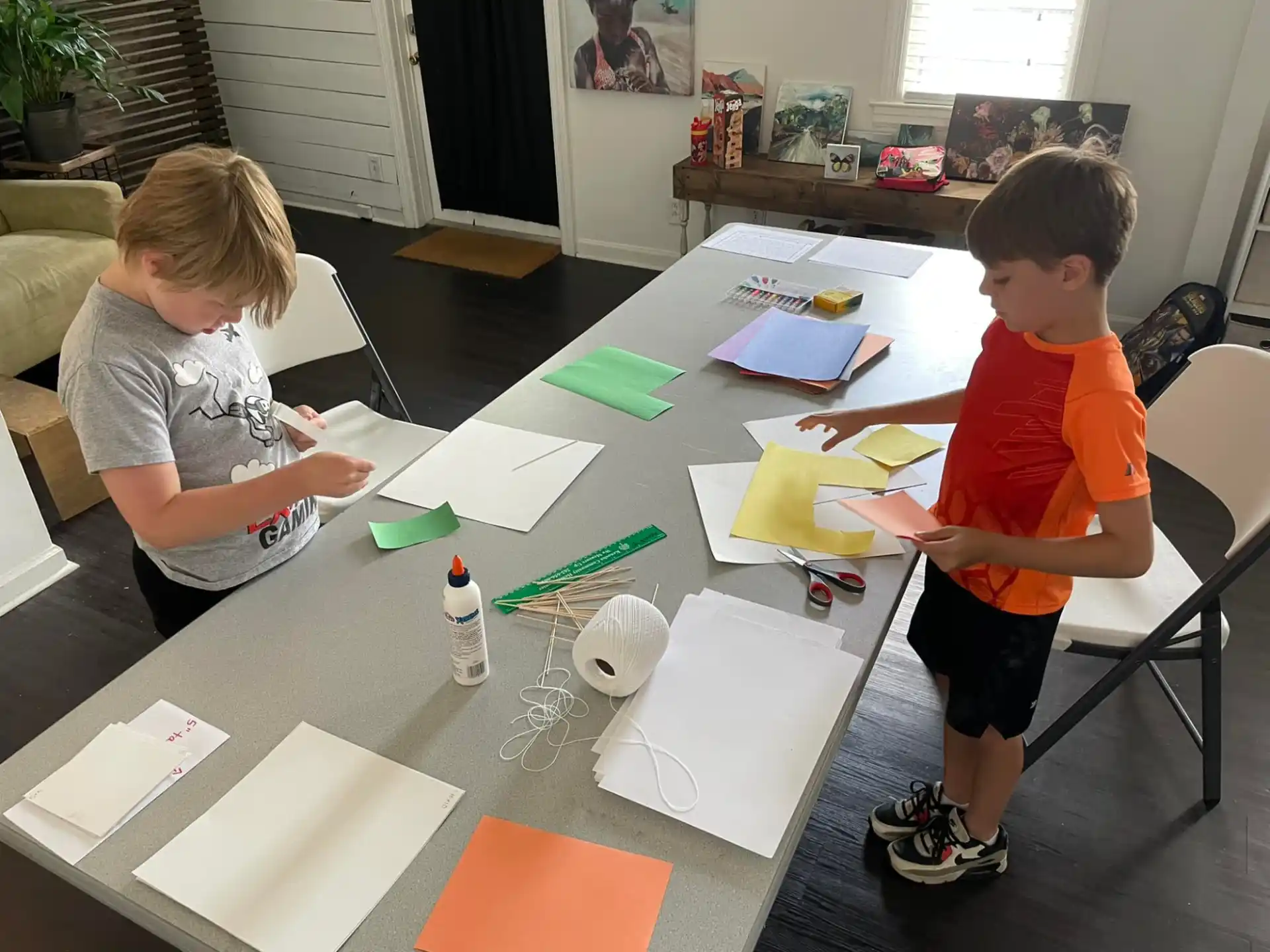 a couple of boys sitting at a table with papers and pencils