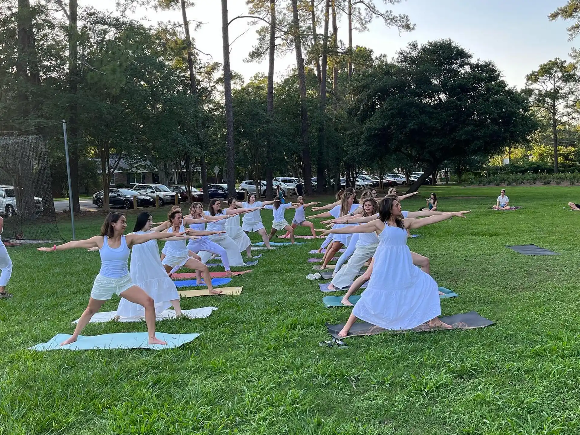 a group of people sitting on mats in a grassy area with trees
