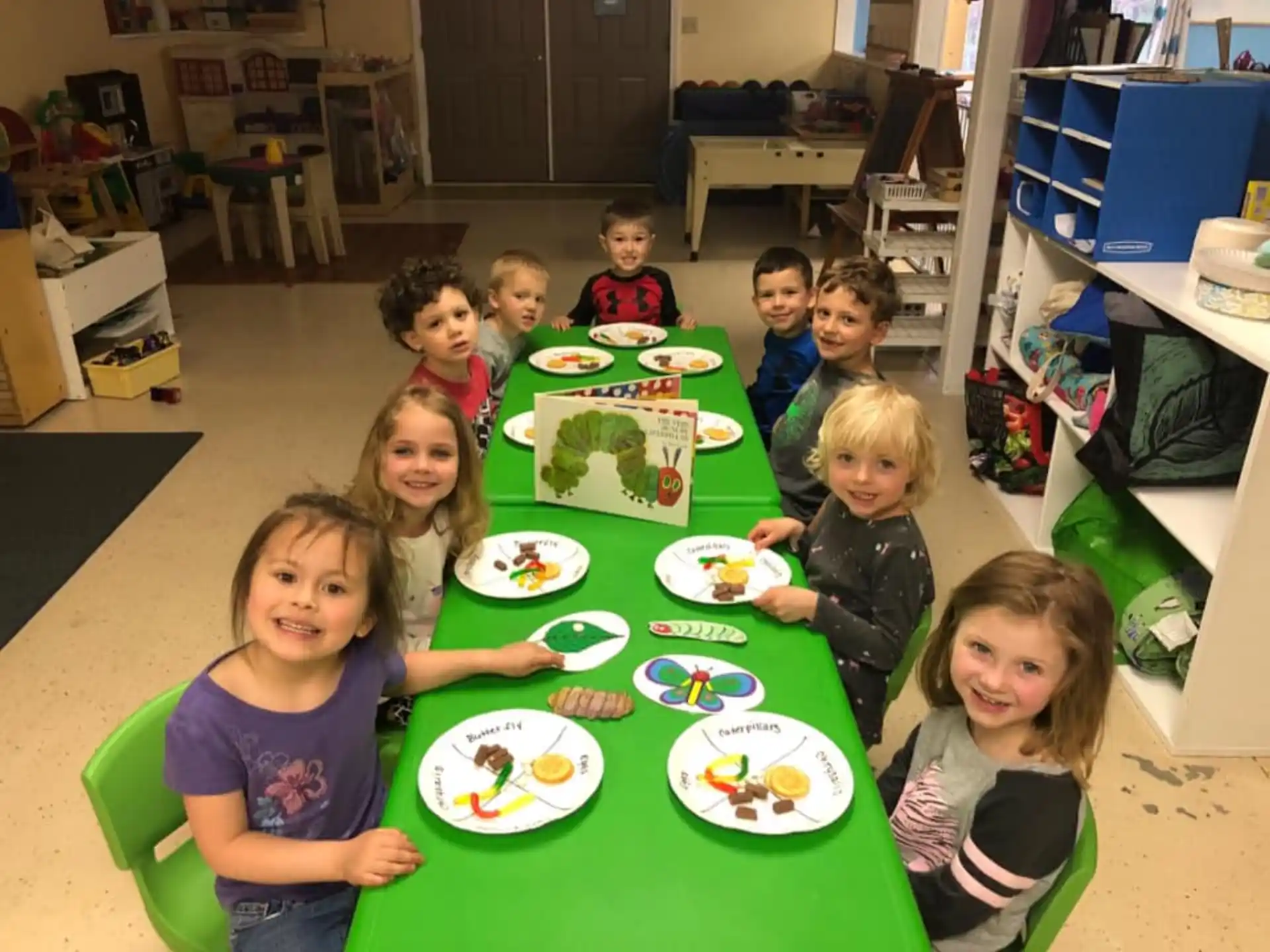 a group of children sitting at a table with plates of food