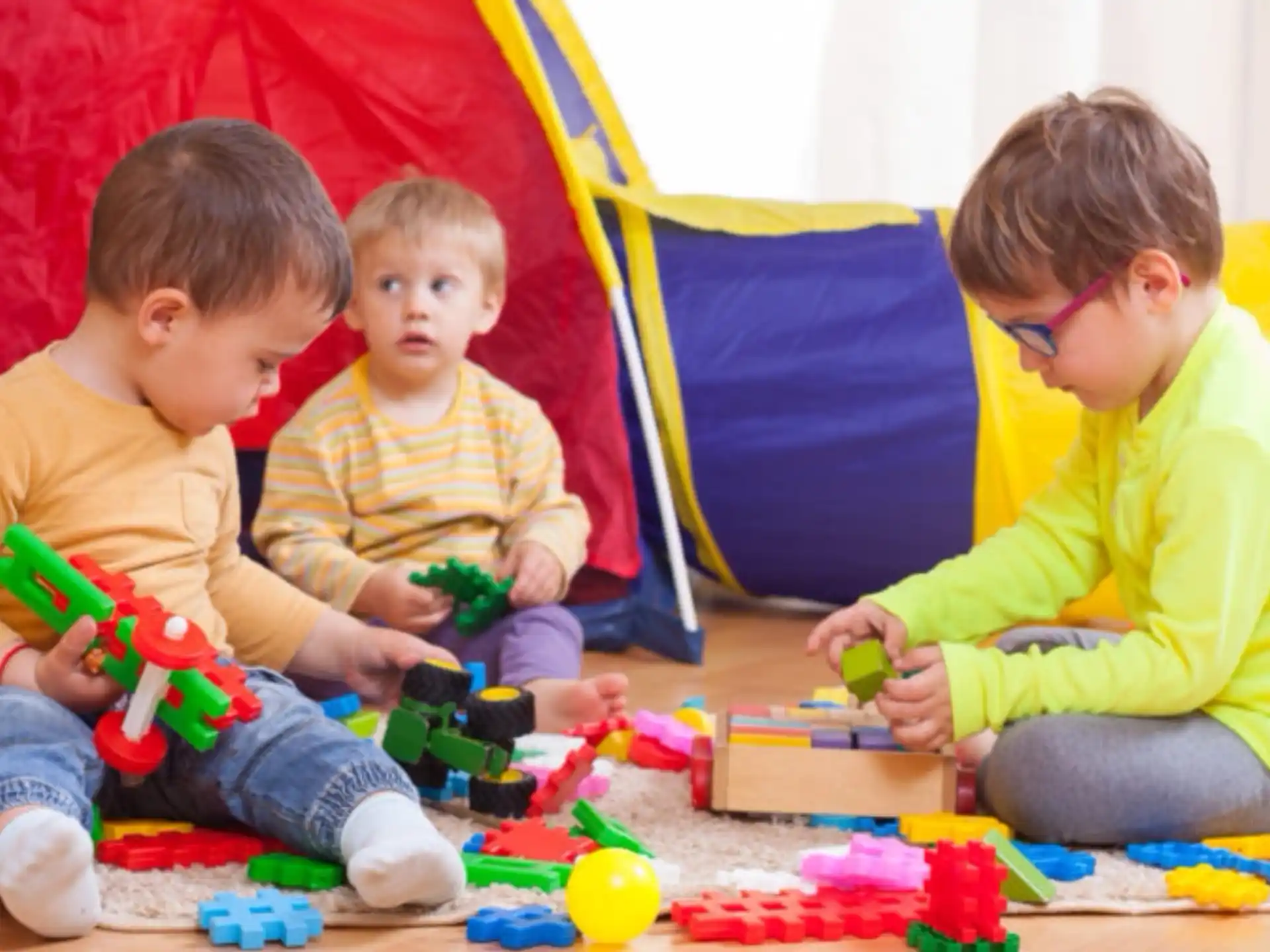 a person and two boys playing with toys on a wood floor
