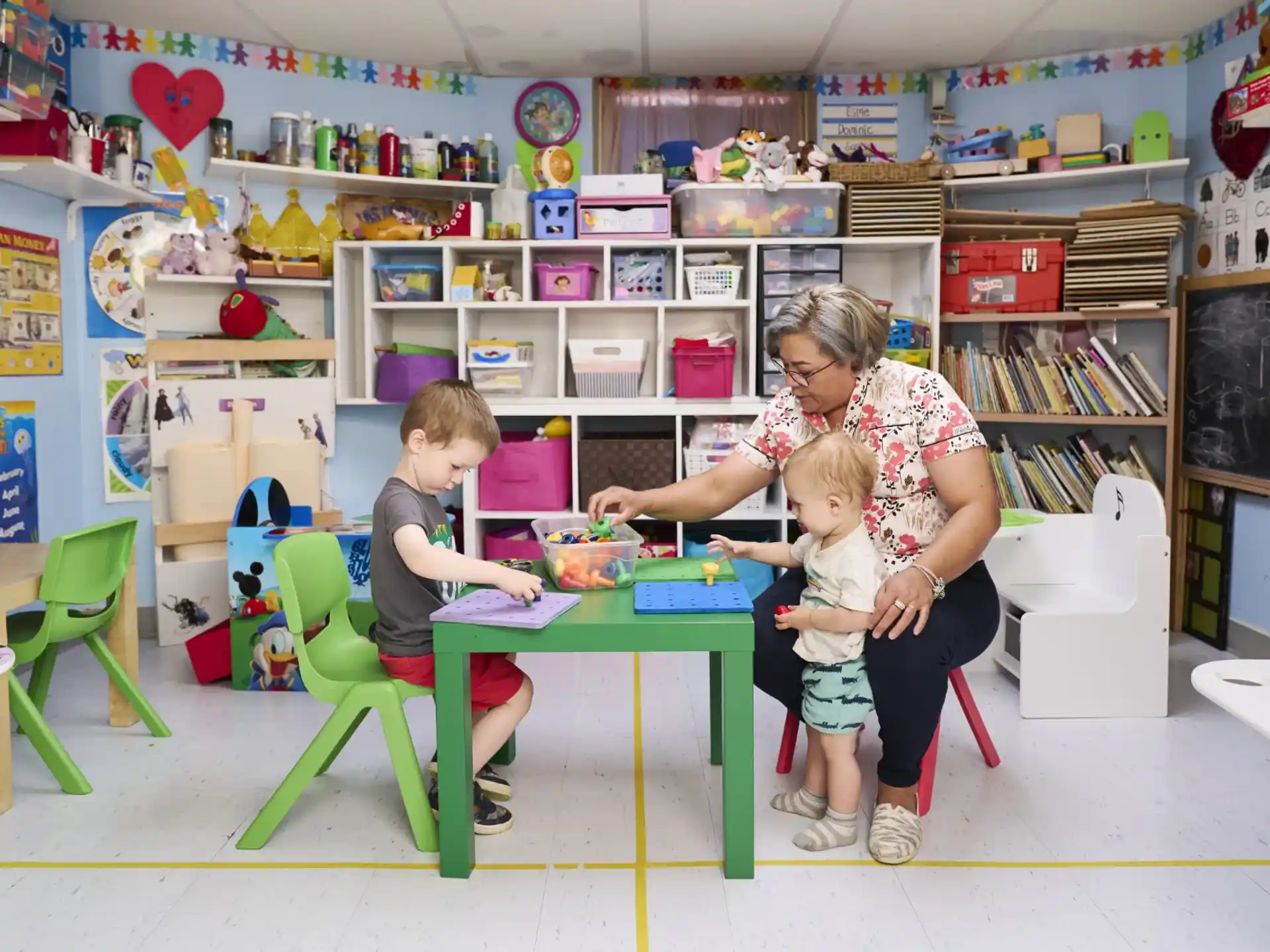 a person and a couple of children sitting at a table in a classroom