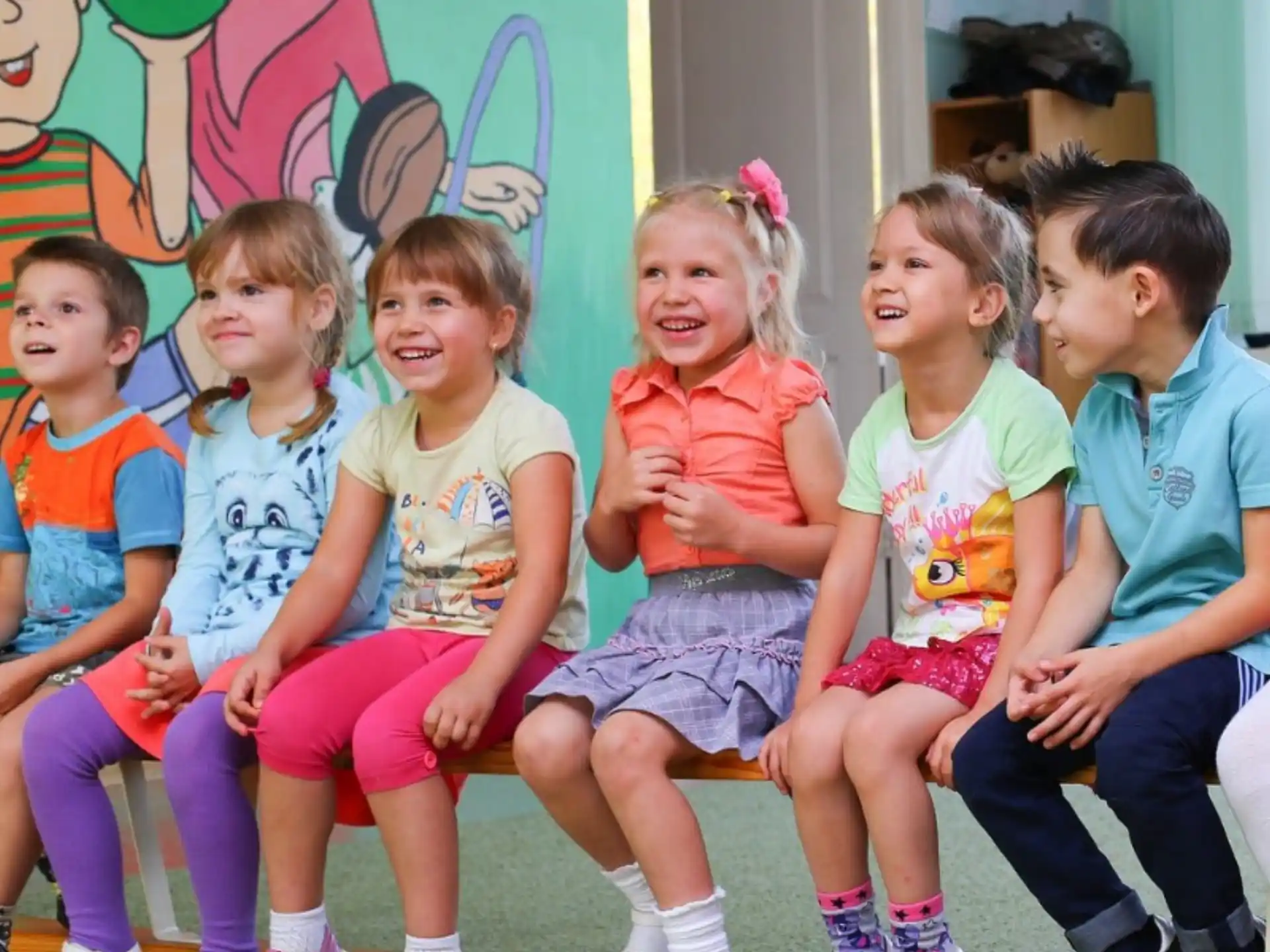a group of children sitting on a bench in front of a wall