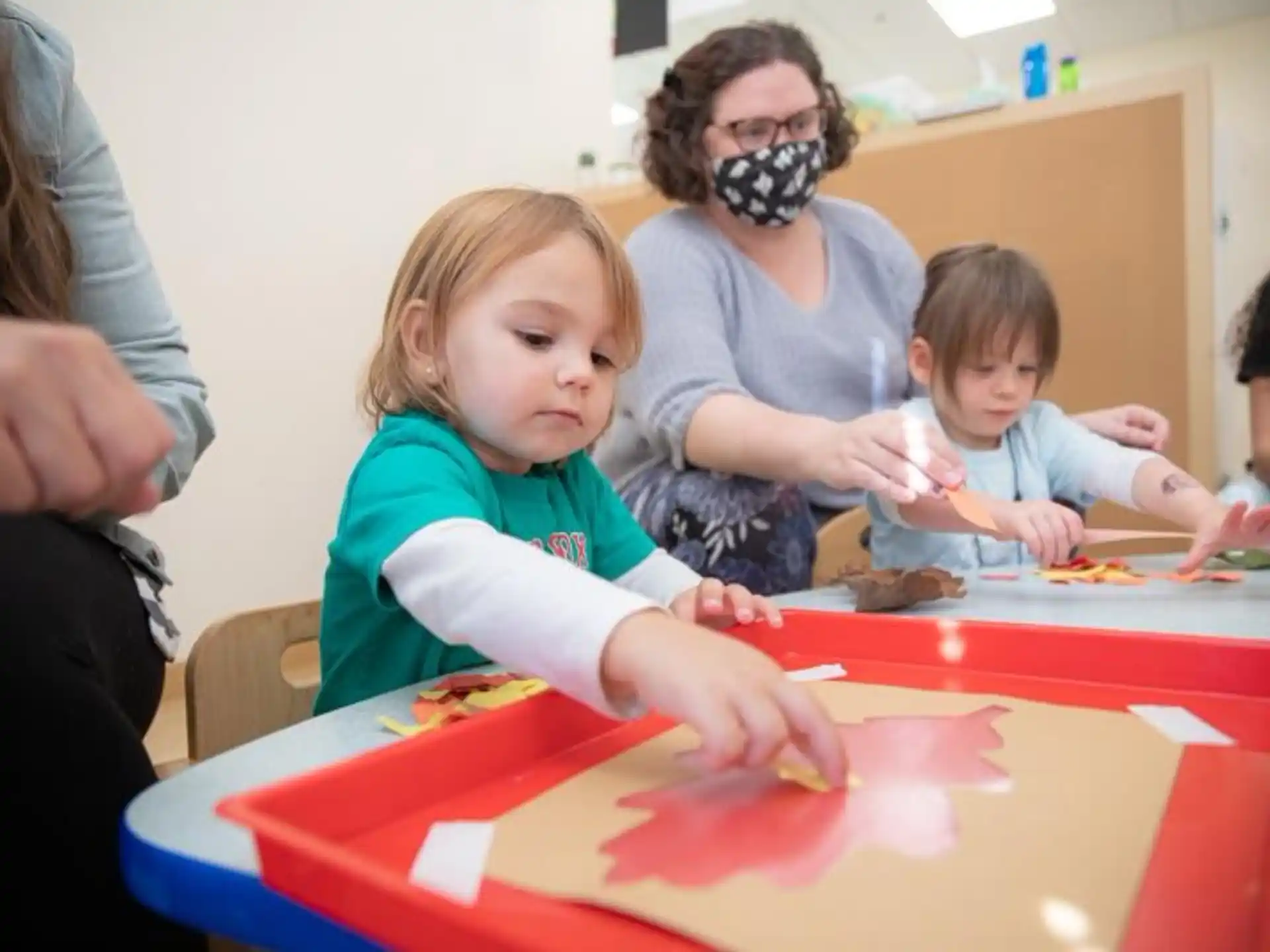 a group of children sitting at a table with a person in a mask