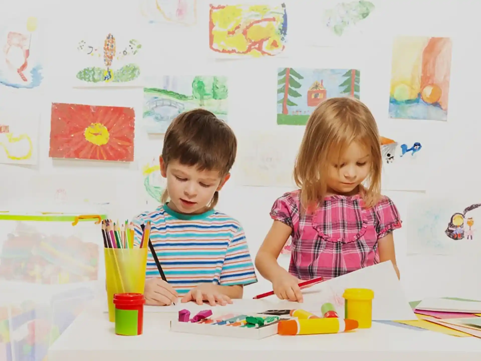 a boy and girl sitting at a table with colored pencils