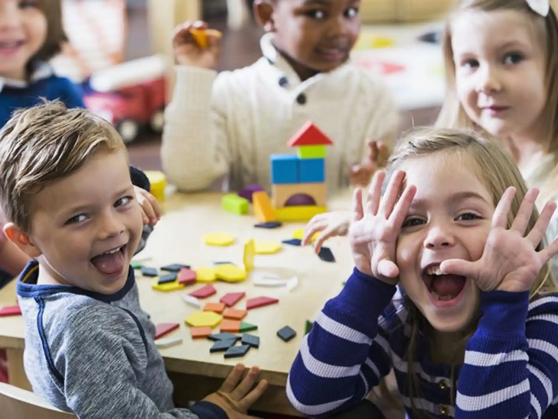 a group of children sitting at a table with their hands up