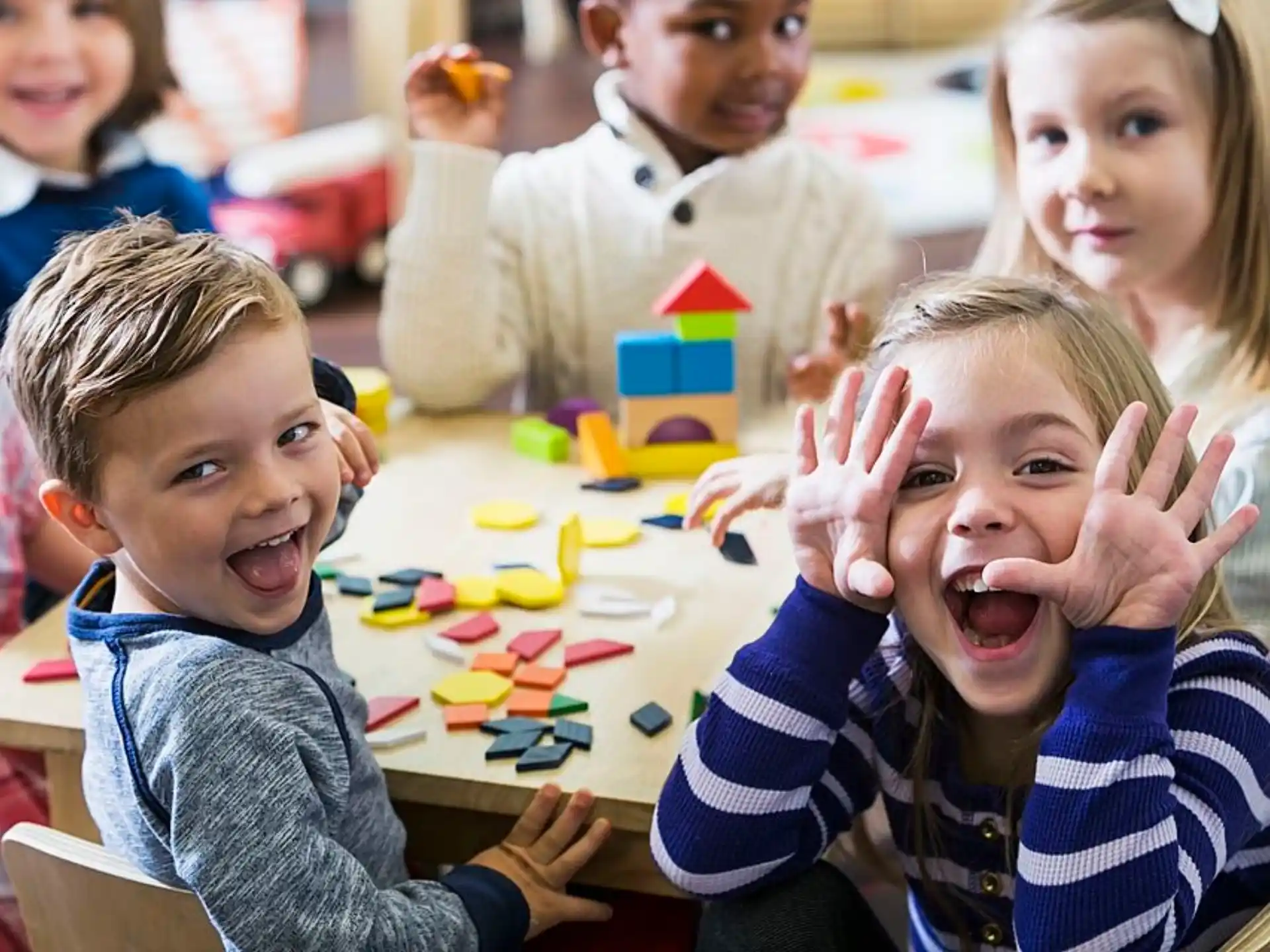 a group of children sitting at a table with their hands up