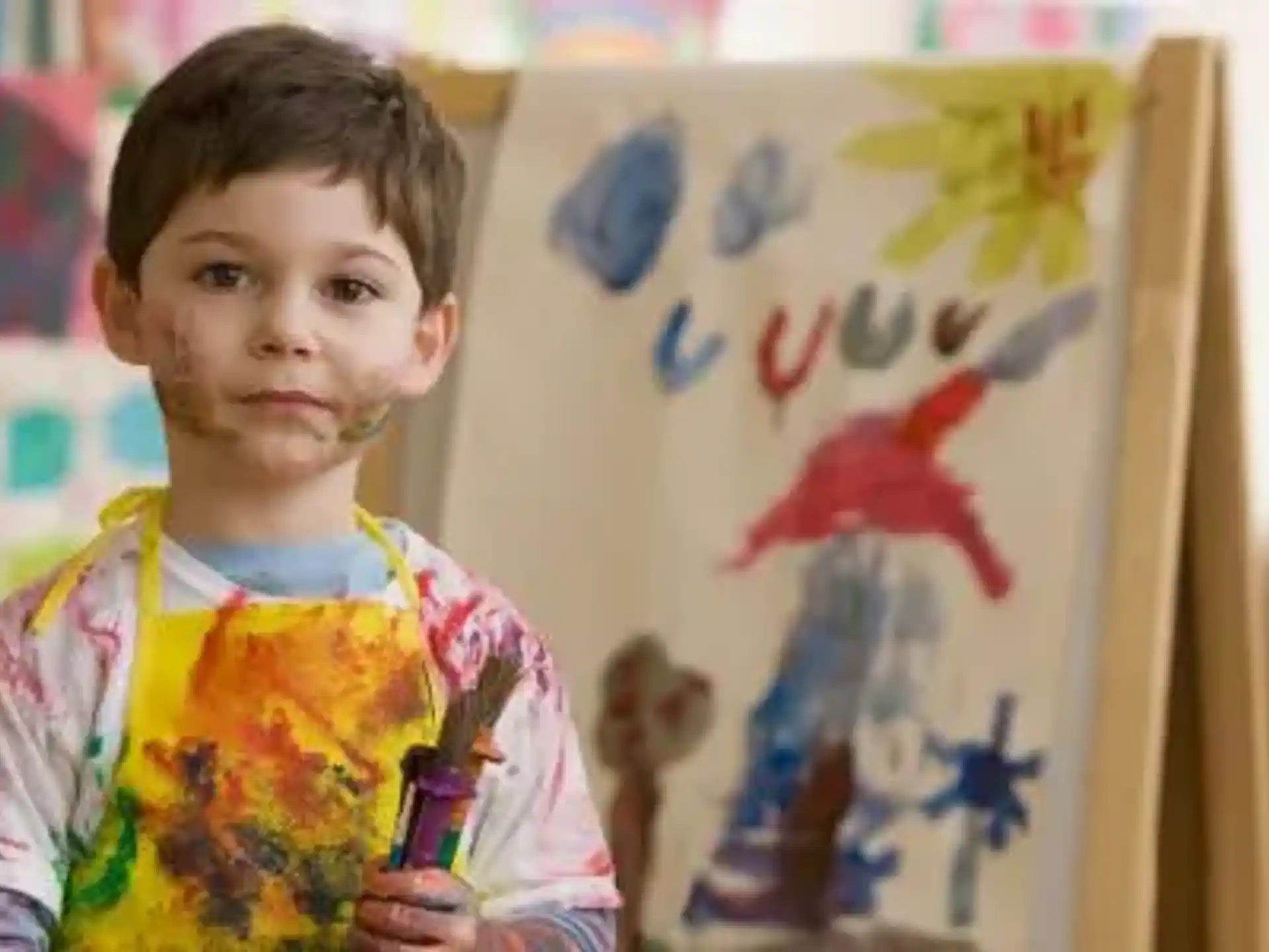 a child standing in front of a white board with colorful drawings