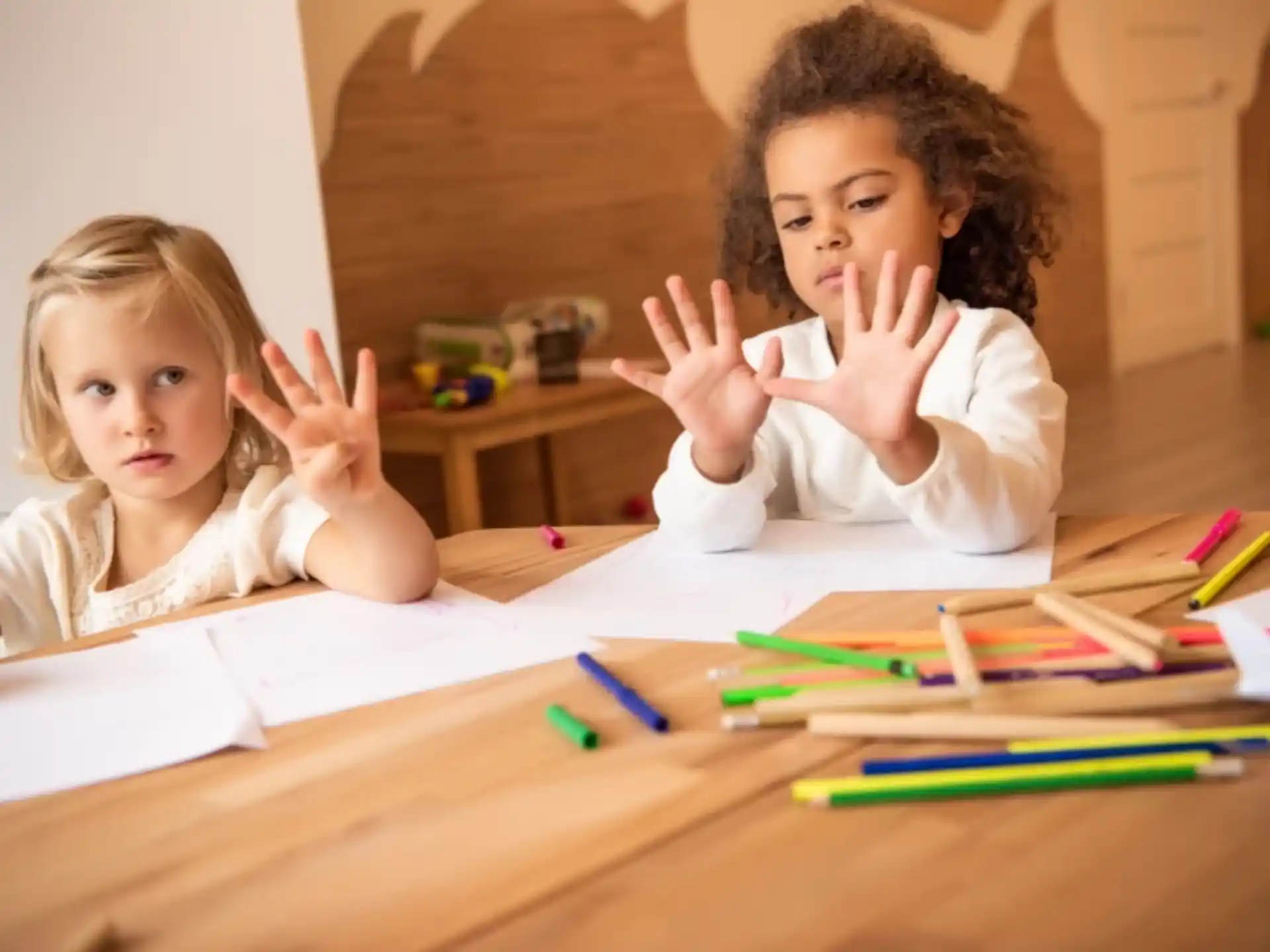 a couple of children sitting at a table with their hands up