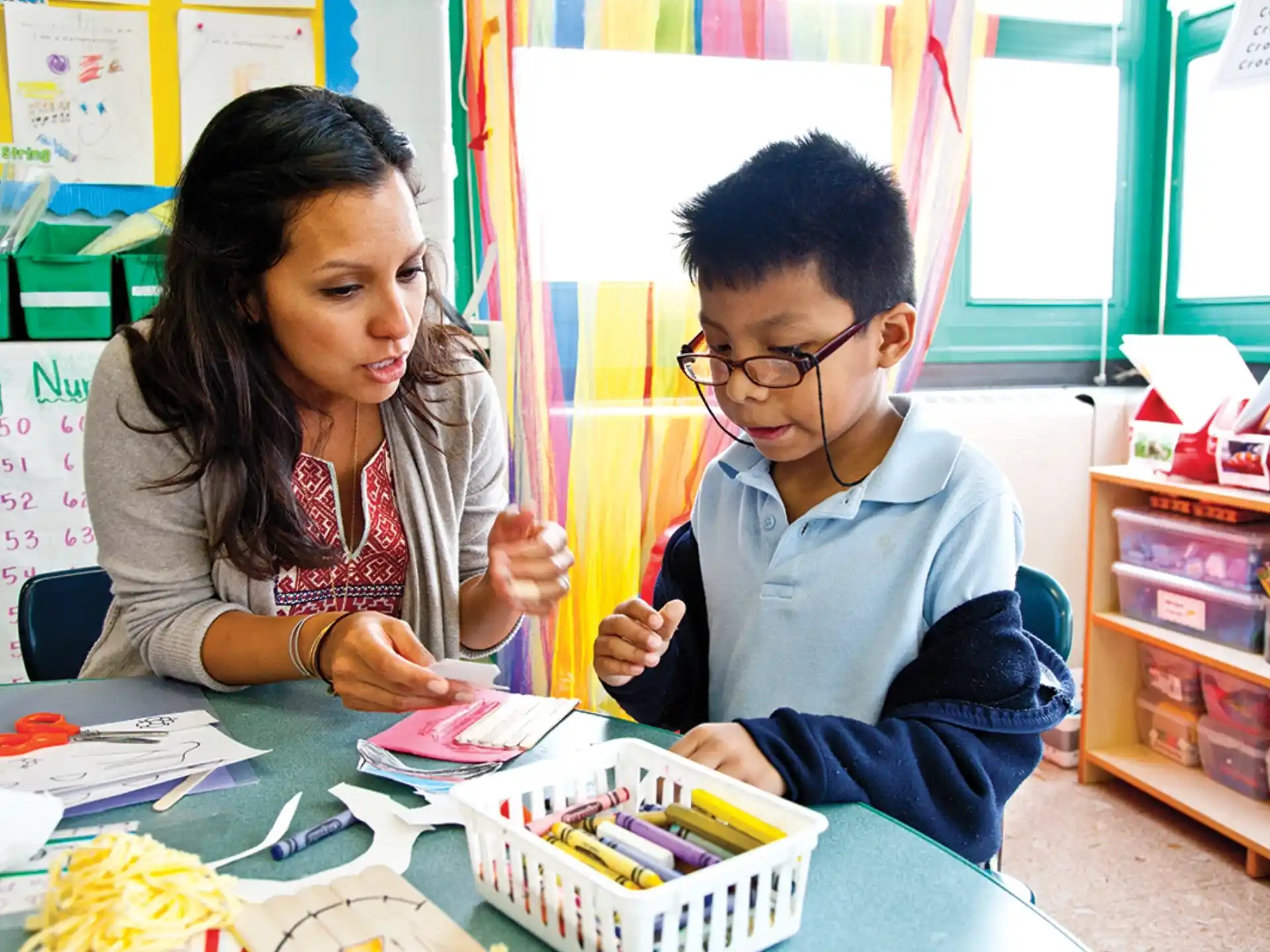 a boy and girl sitting at a table with books and pencils