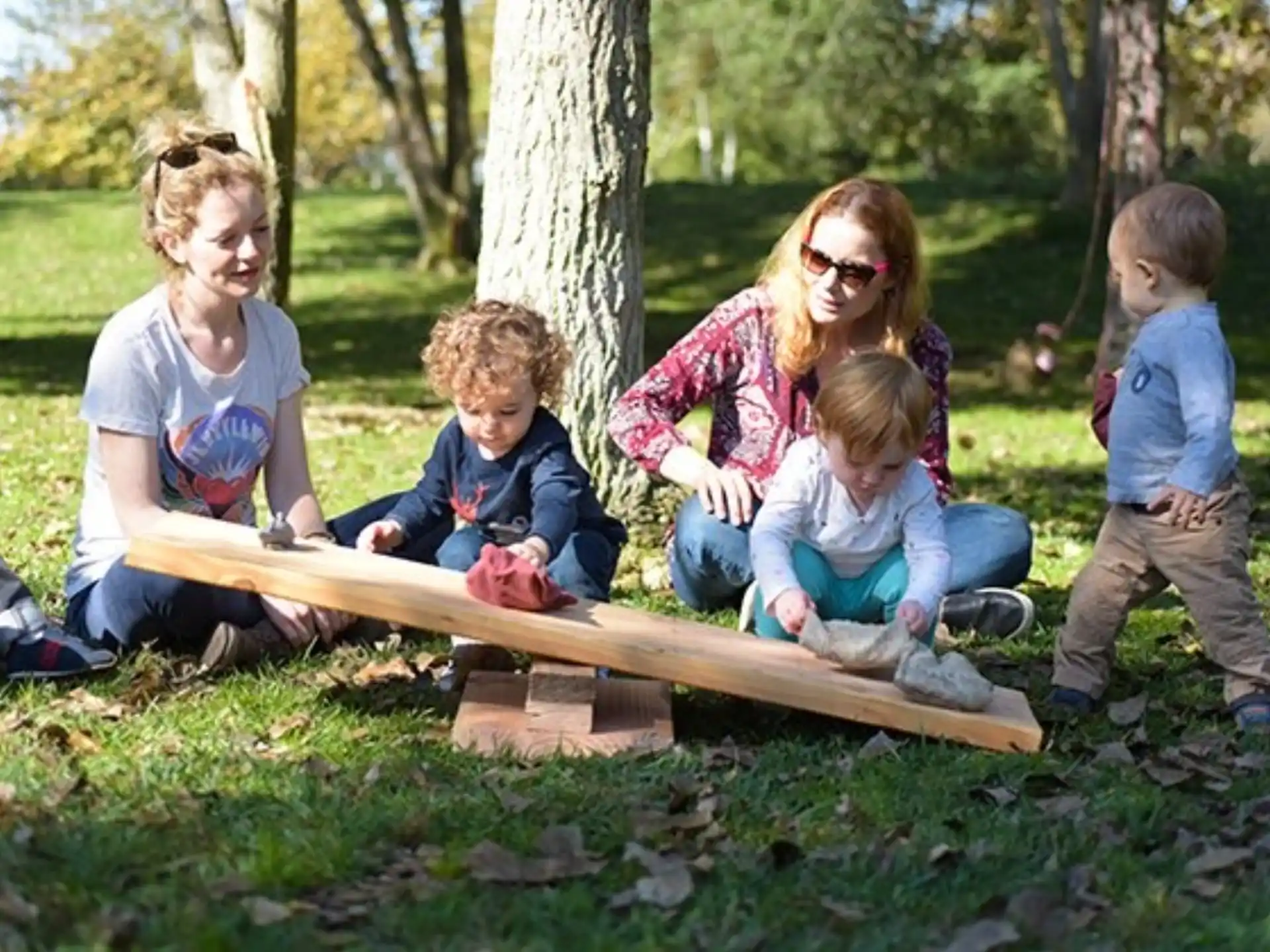 a person and several children sitting on a wood bench in a park