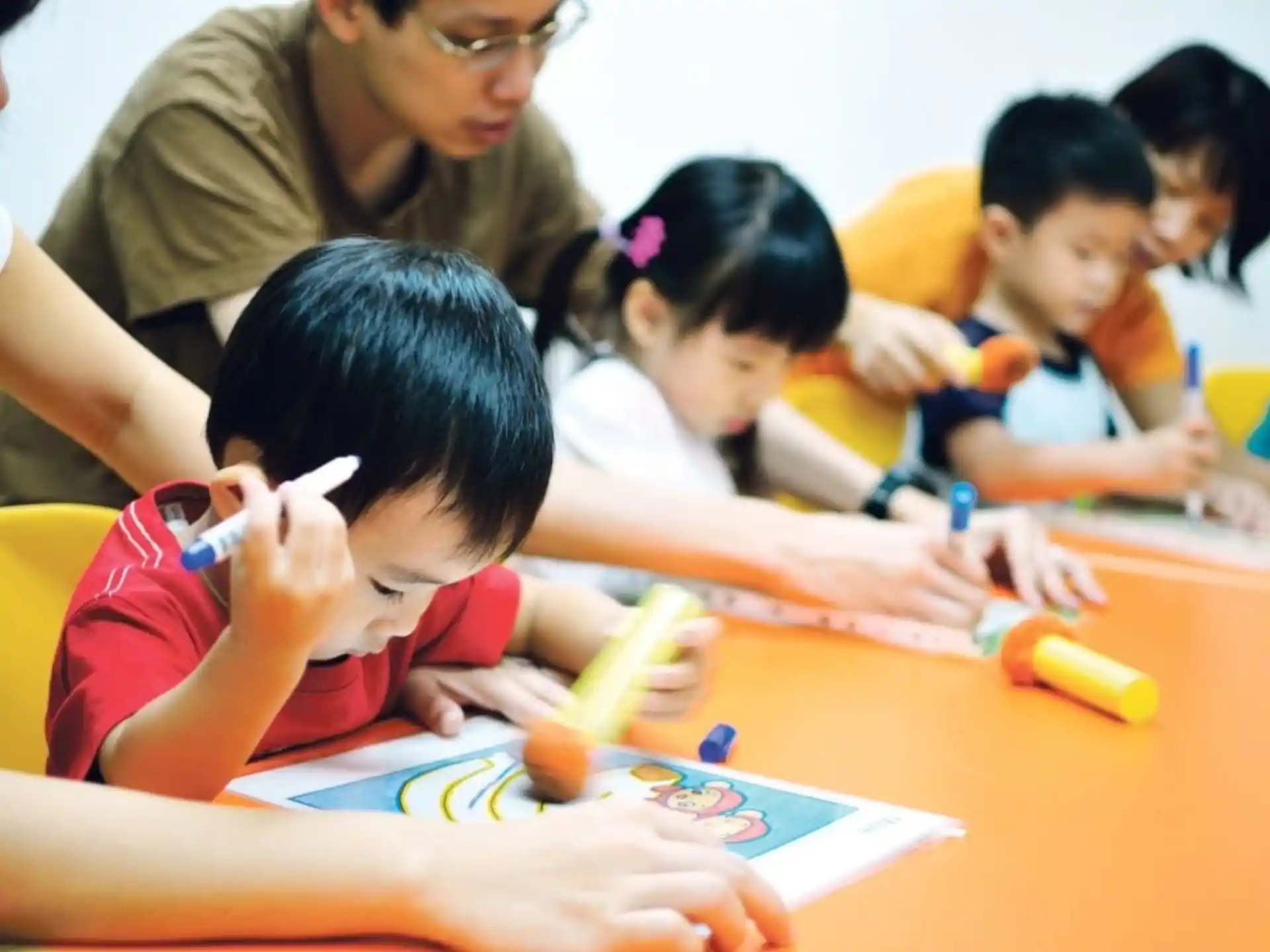 a group of children sitting at a table writing on paper