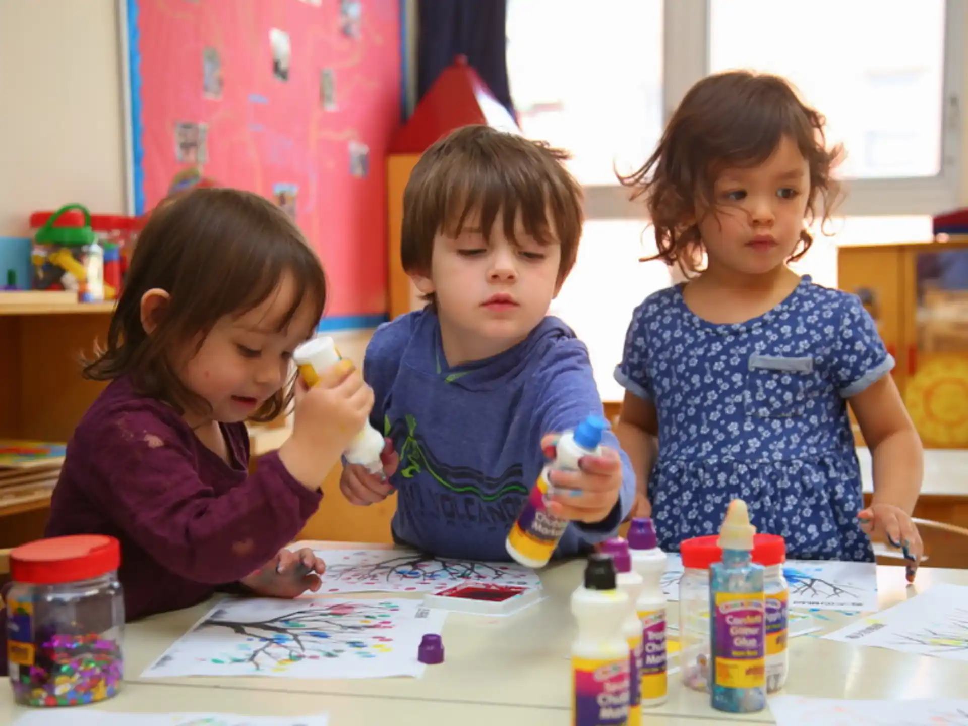 a group of children sitting at a table with paintbrushes