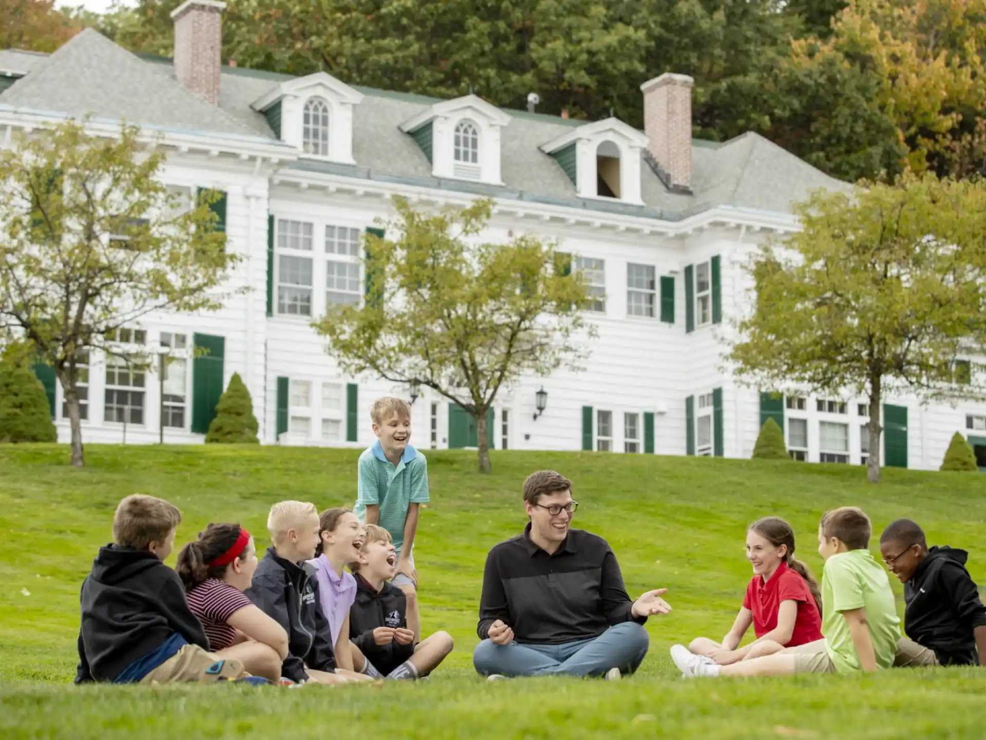 a group of people sitting on the grass in front of a white house