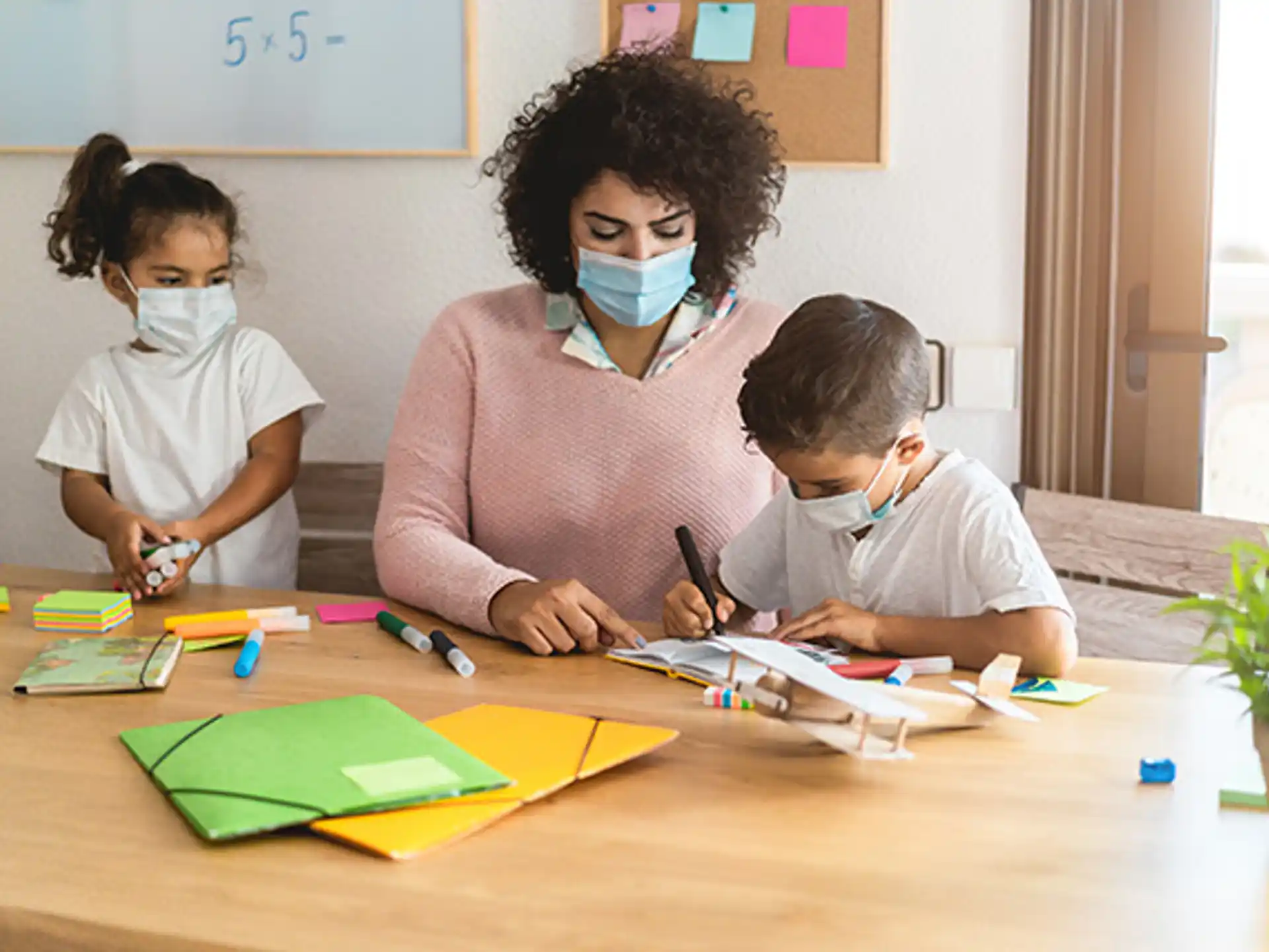 a person and a couple of children wearing masks and sitting at a table