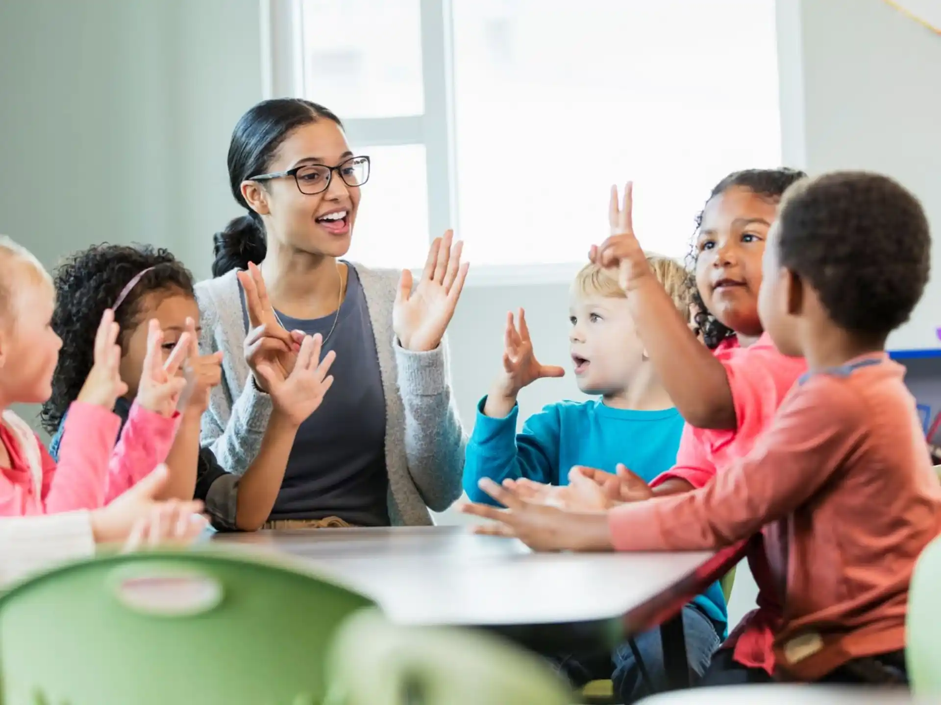a group of children sitting at a table with their hands up
