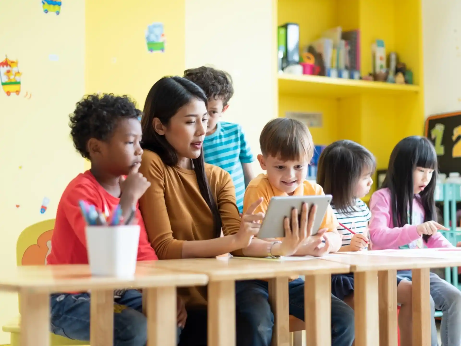 a group of children sitting at a table looking at a tablet