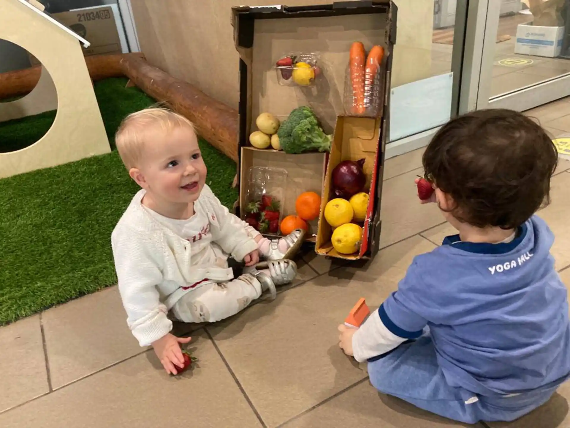 a couple of babies sitting on a tile floor next to a refrigerator