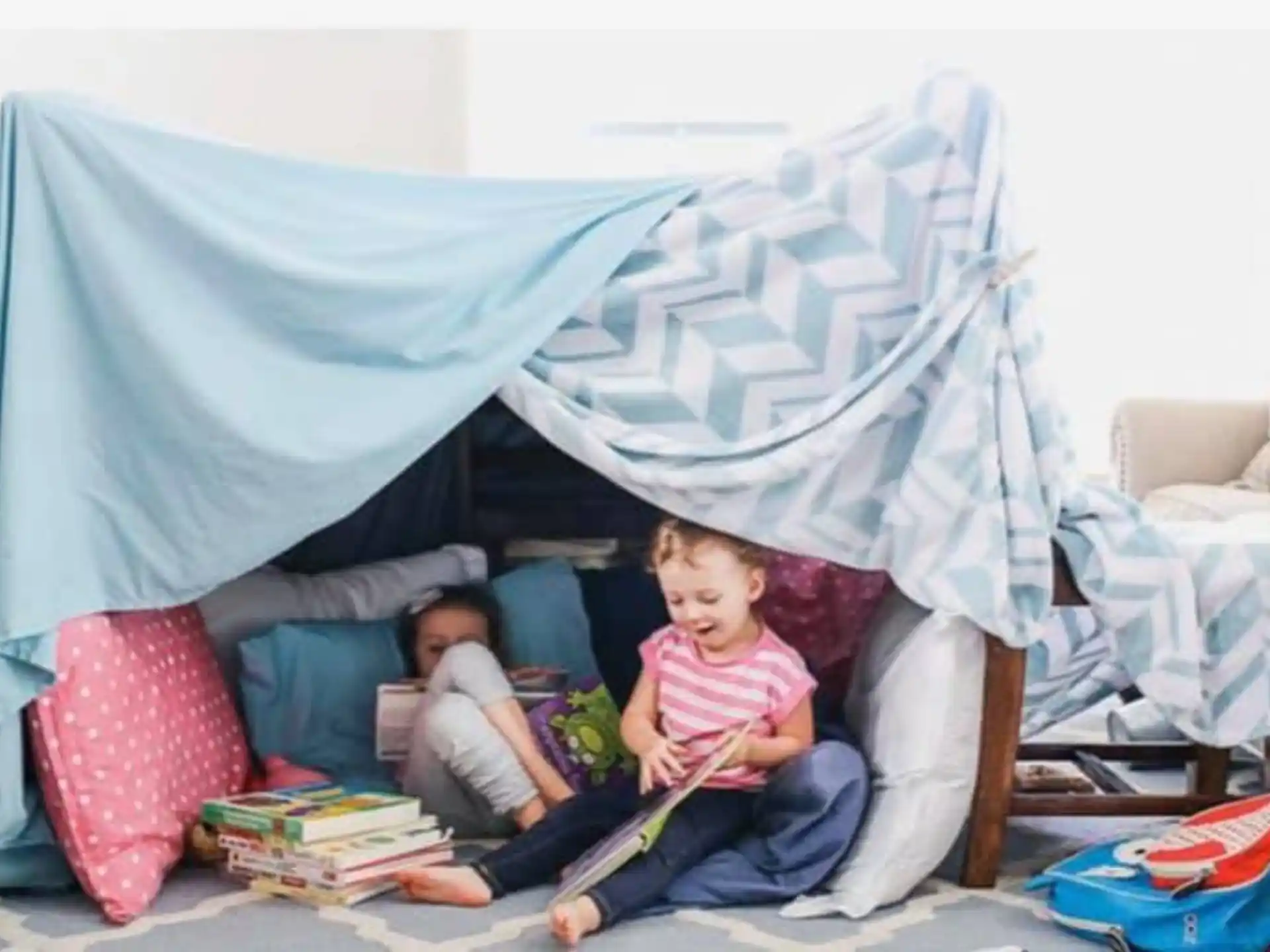 a couple of children sitting on a couch with a blue tent behind them