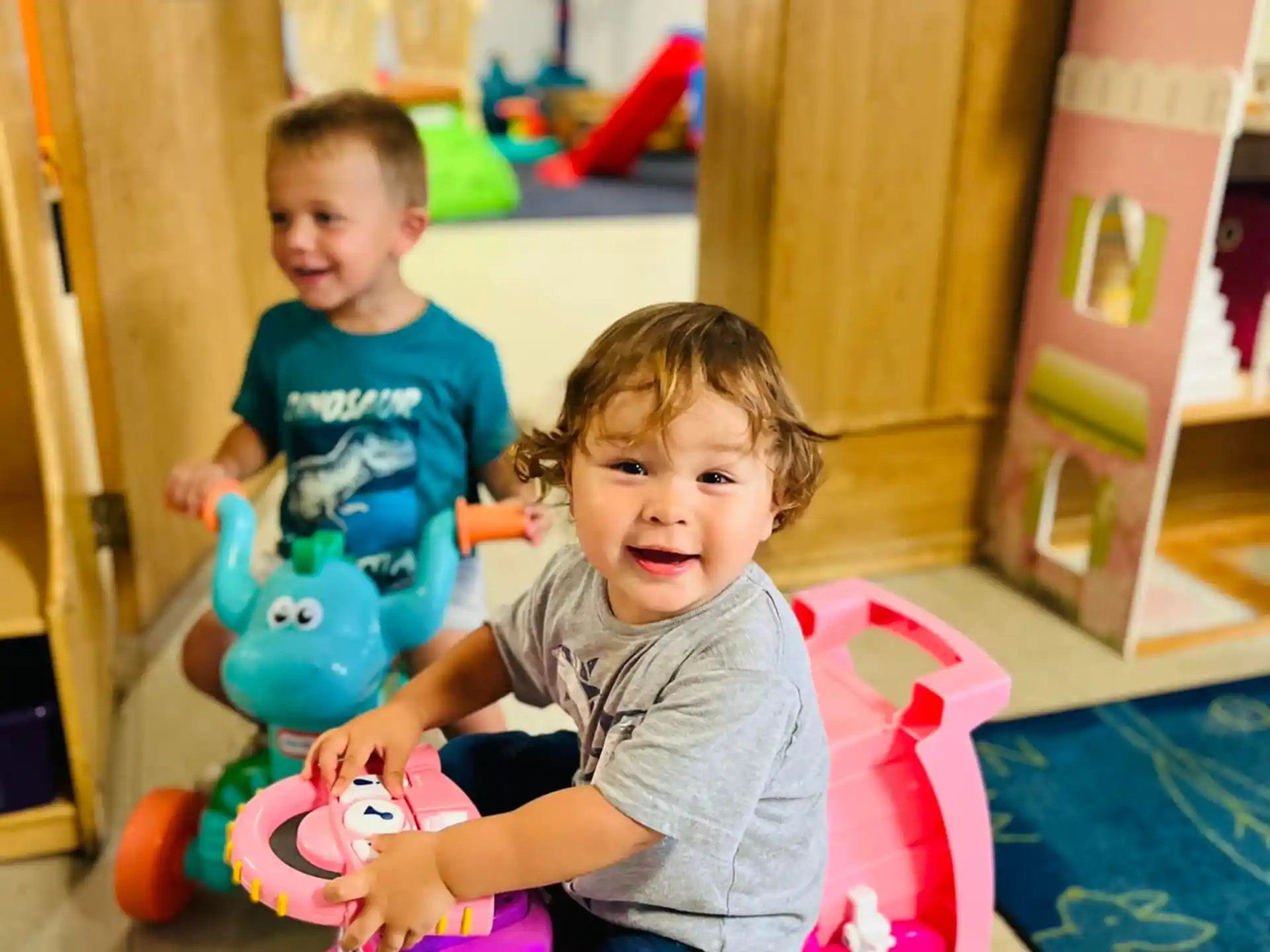 a couple of kids sitting on a toy car in a room
