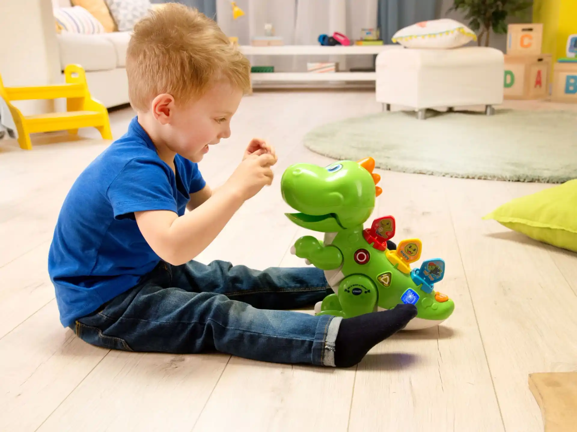 a boy sitting on the floor next to a toy dinosaur
