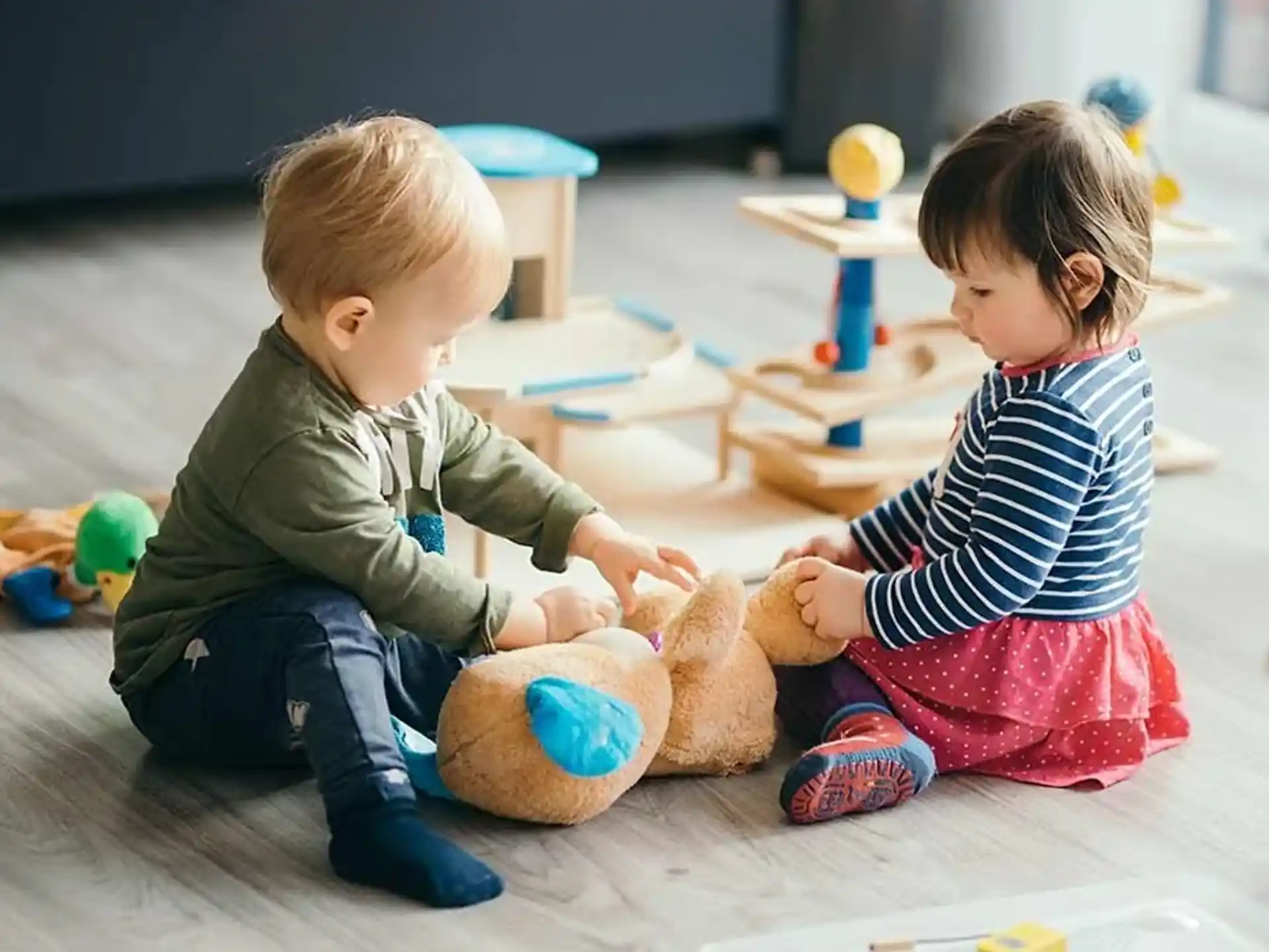a couple of kids playing with a teddy bear