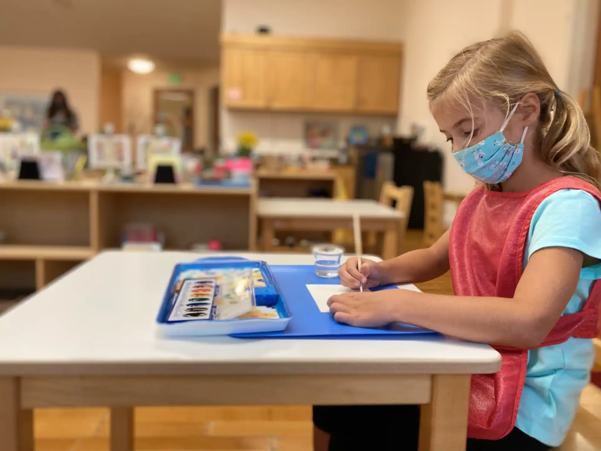 a young girl wearing a mask and a mask writing on a blue piece of paper
