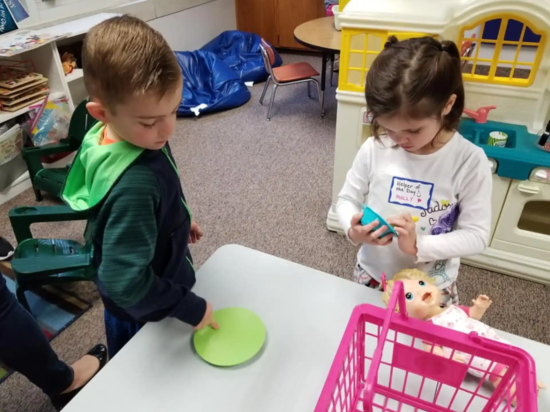 a couple of kids sit at a table with a doll