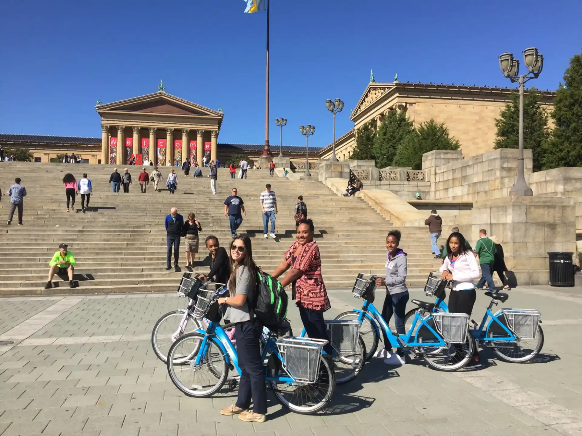 a group of people with bicycles in a courtyard with a building in the background