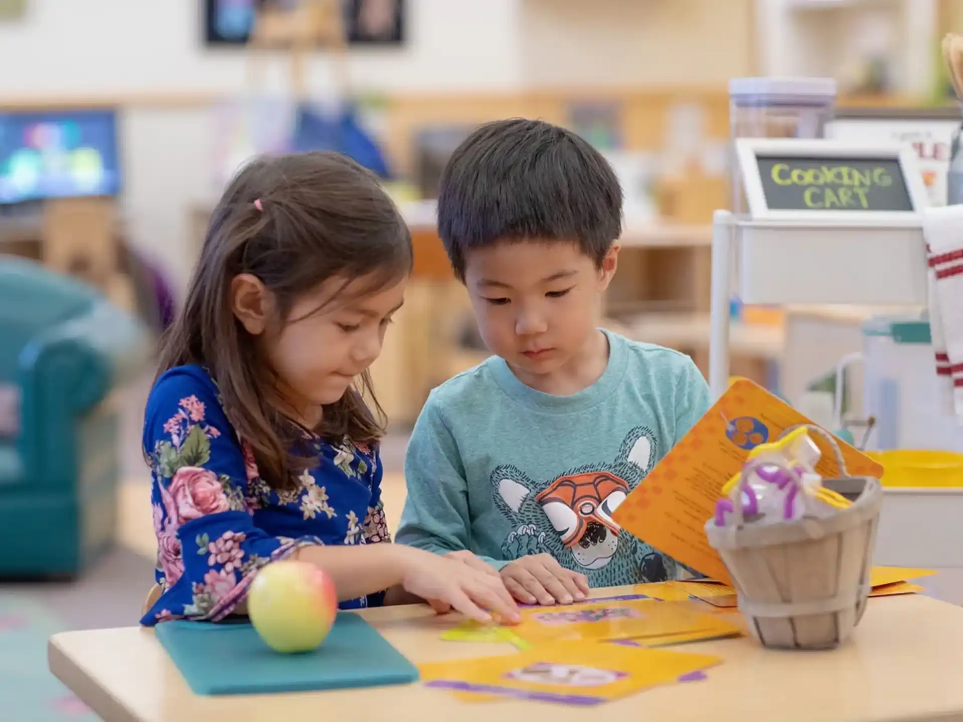 a young boy and girl sitting at a table looking at a book