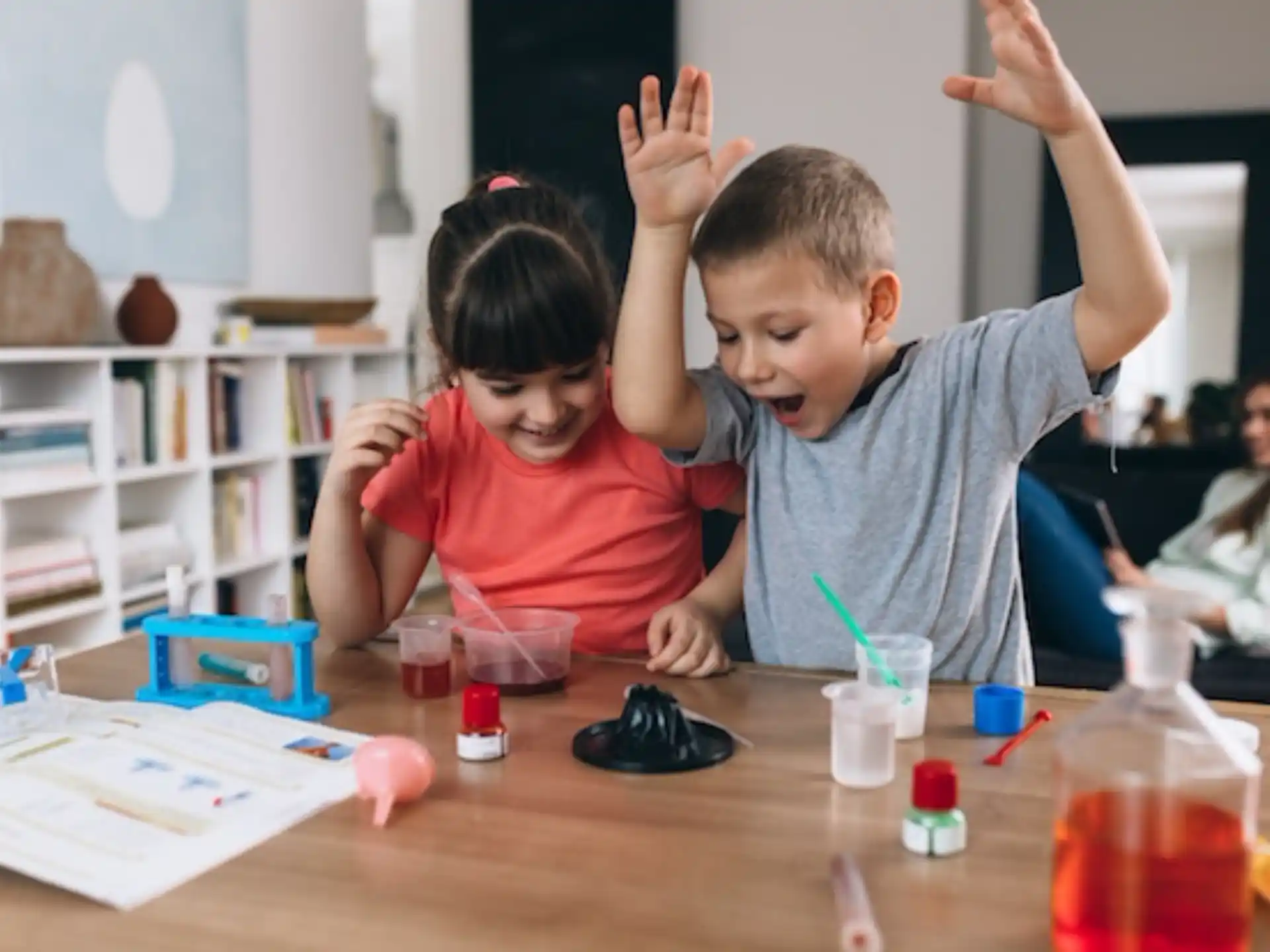a couple of children sitting at a table with their hands up