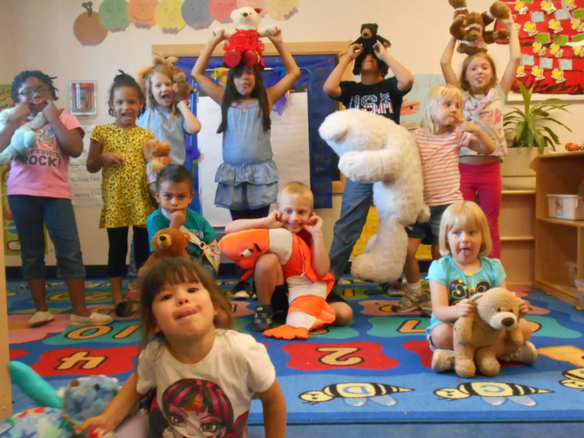 a group of children and adults in a room with stuffed animals