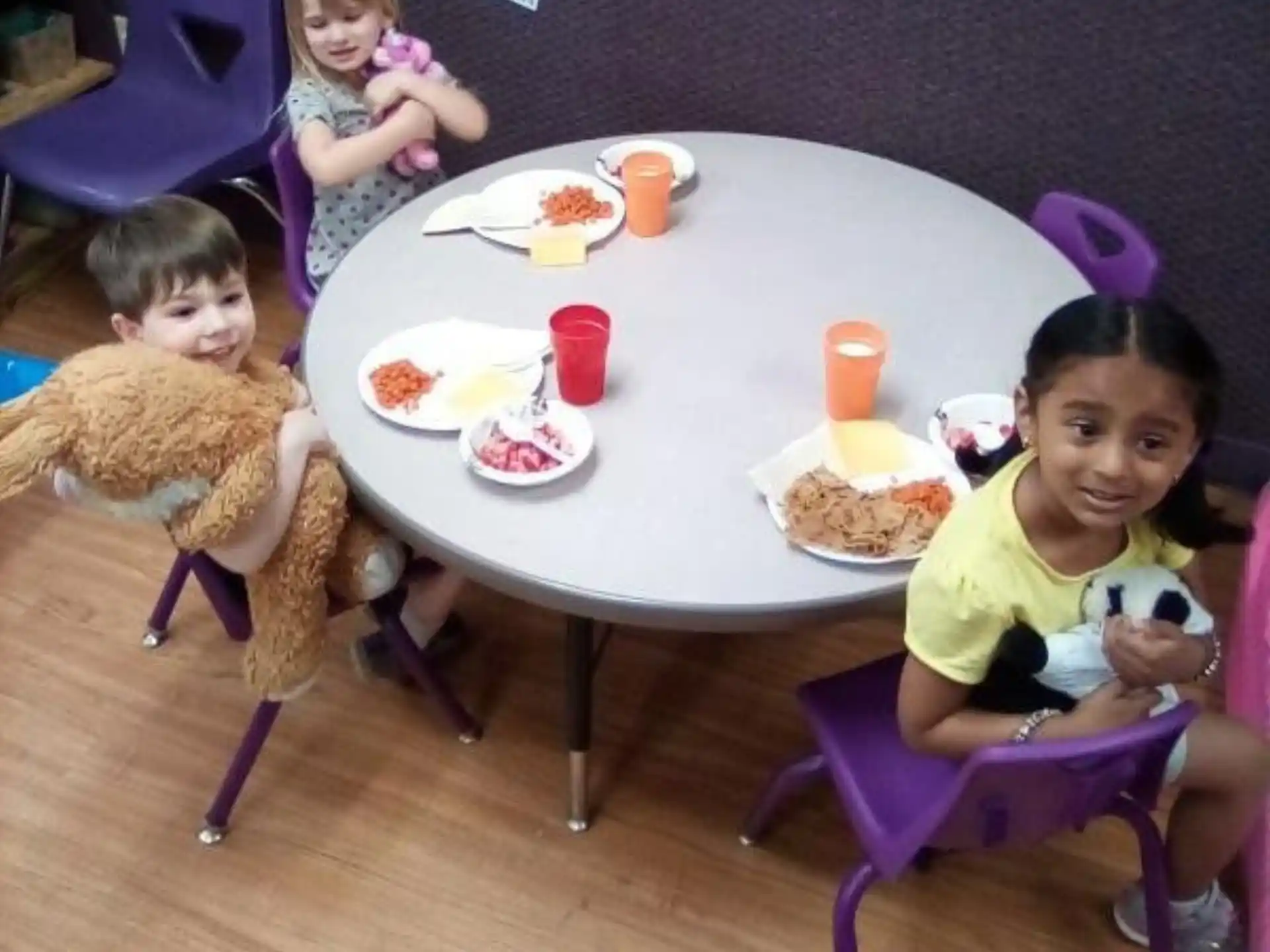 a group of kids sitting at a table with a stuffed animal