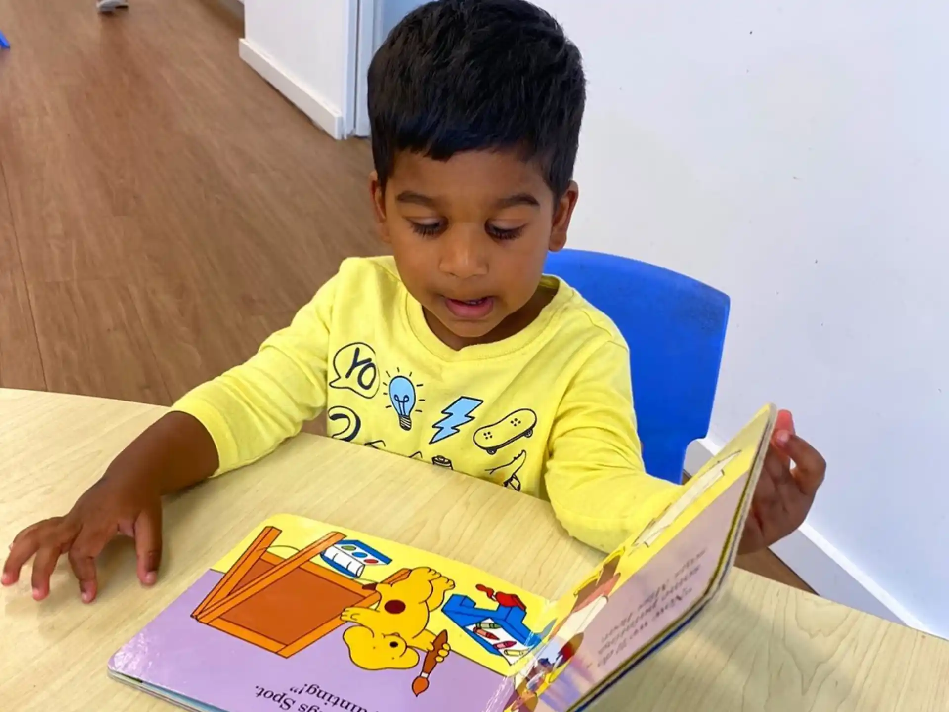 a boy sitting at a table reading a book