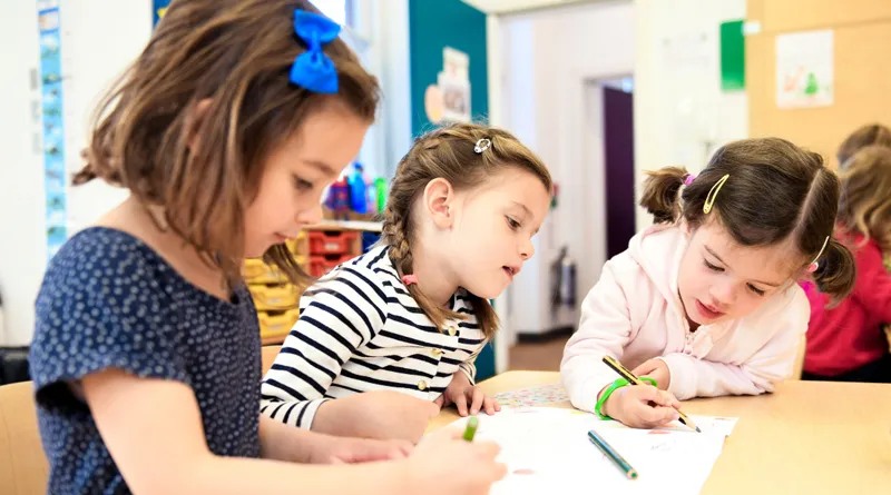 a group of children sitting at a table writing on paper