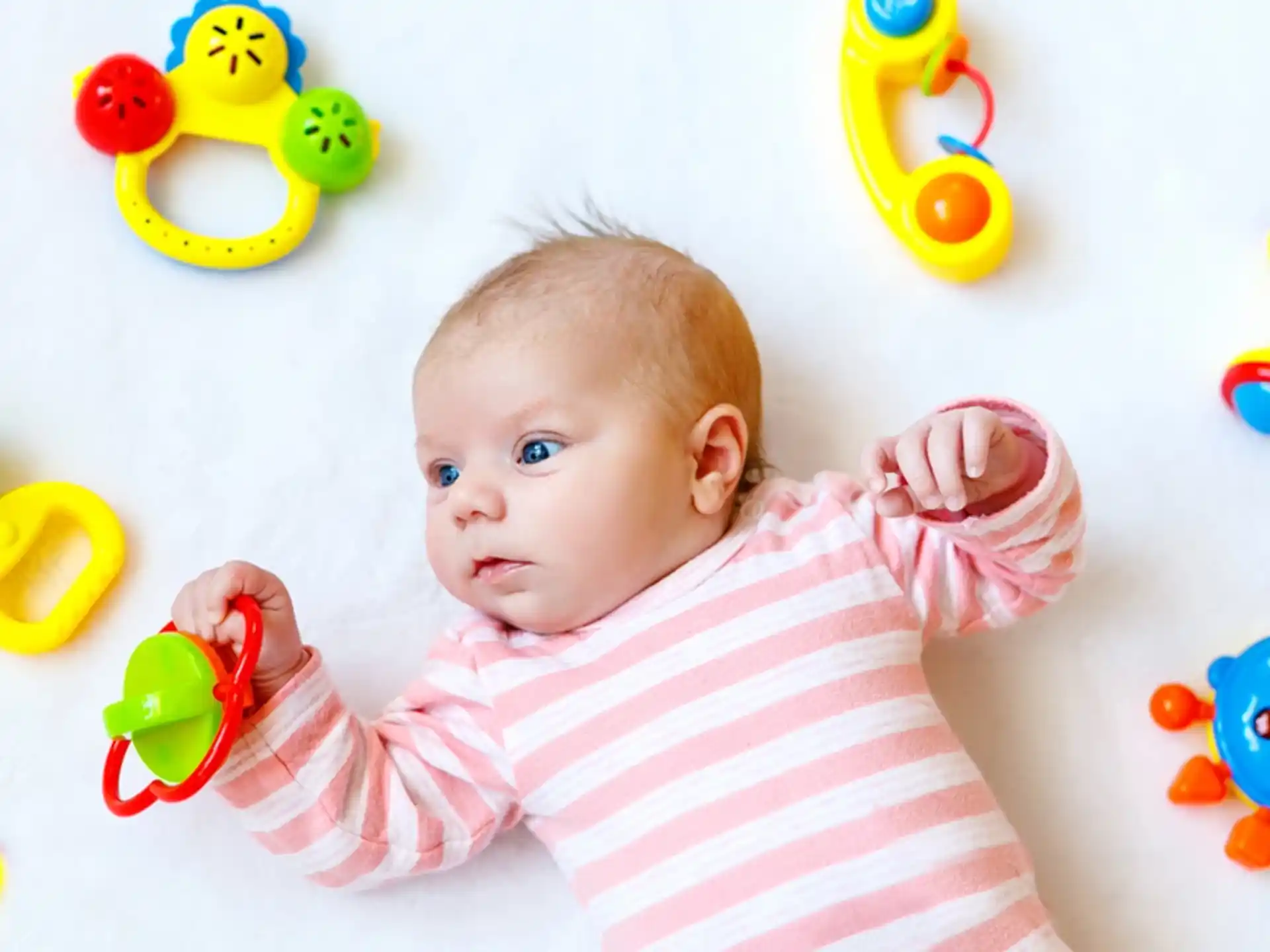 a baby lying on a white surface with toys around it