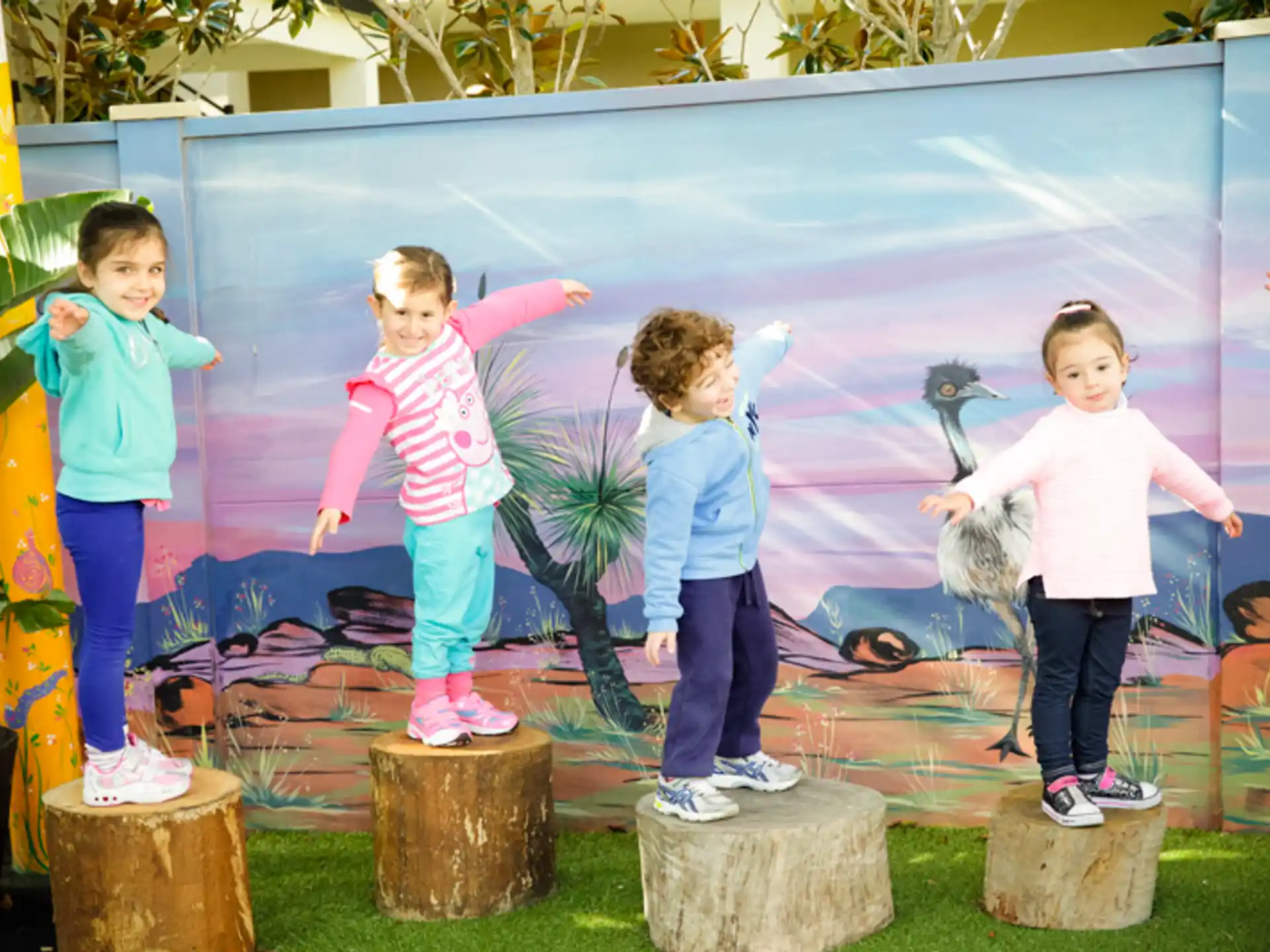 a group of children standing on stumps in front of a painting