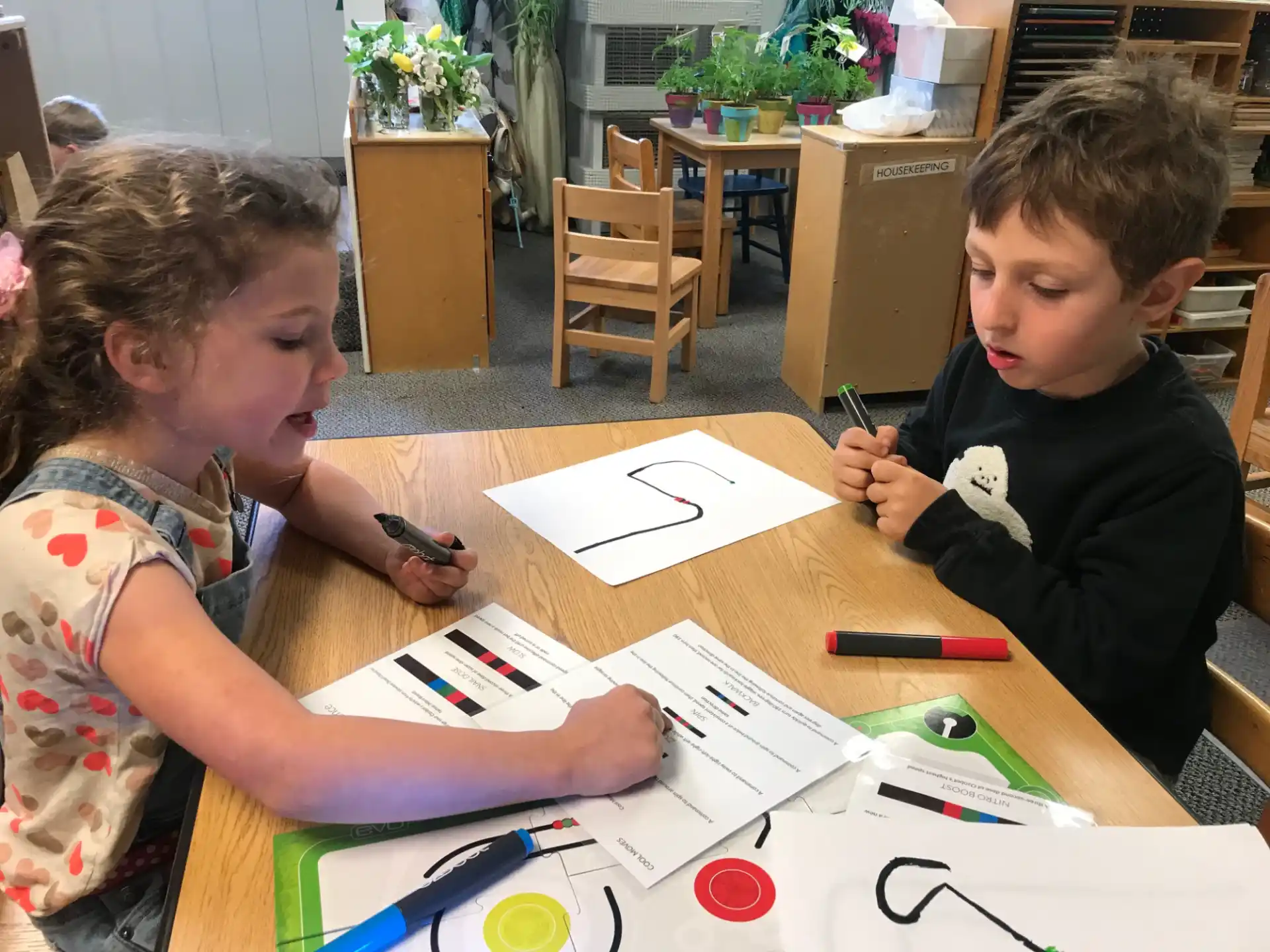 a couple of kids sitting at a table with papers and pens