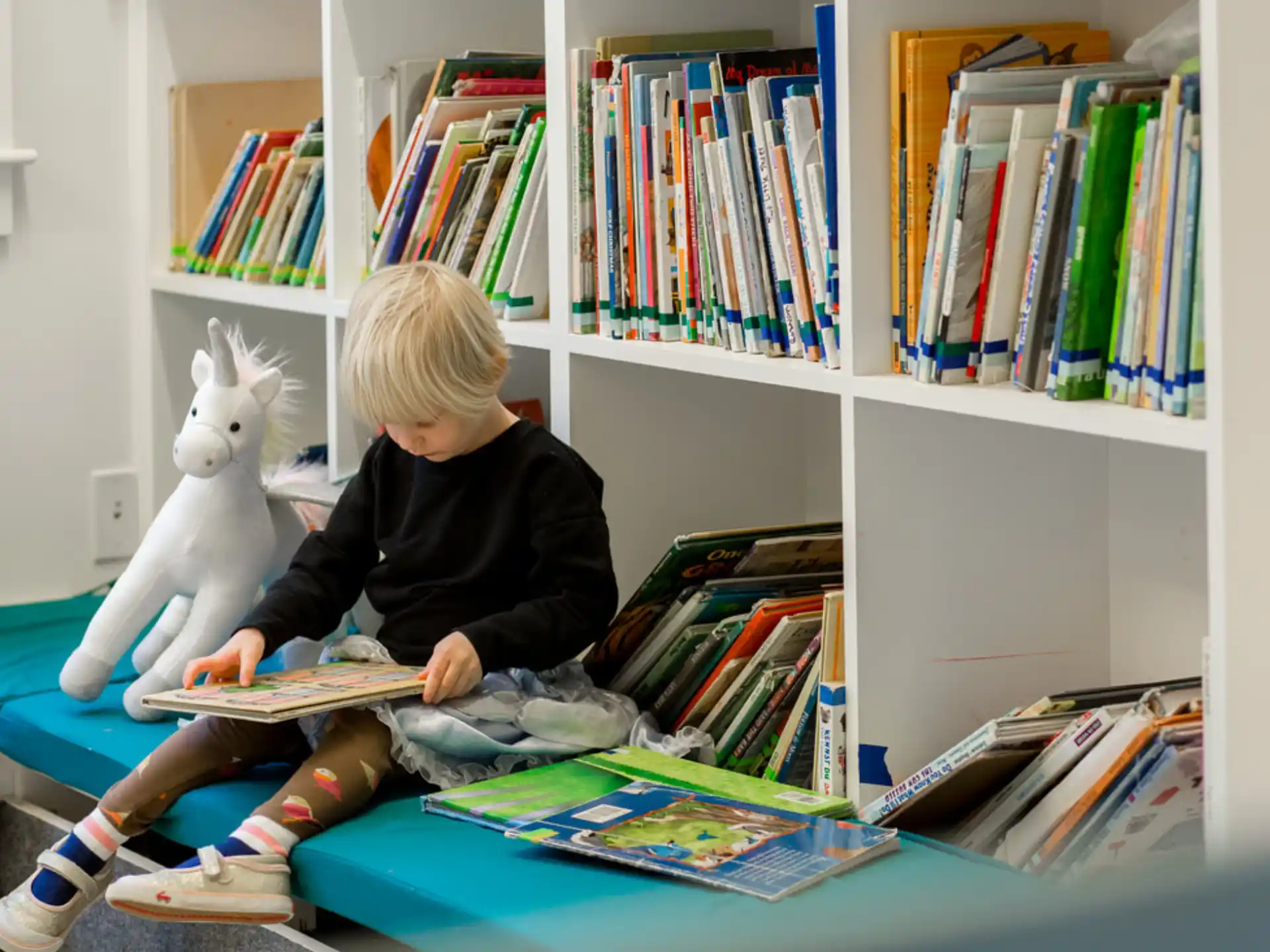 a child sitting at a desk with a book and a stuffed animal
