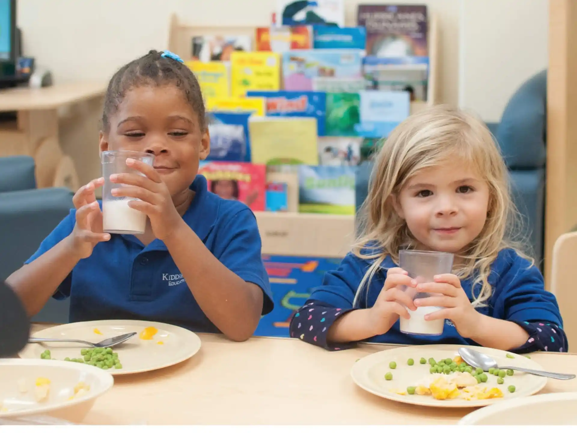 a boy and girl sitting at a table with food and drinks