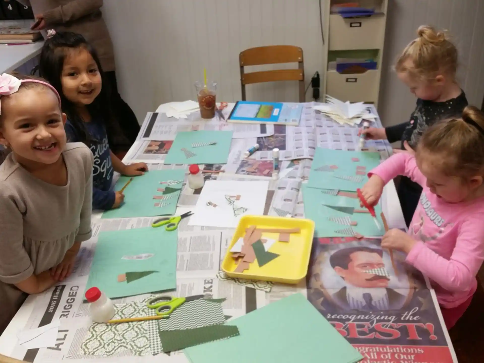 a group of children sitting around a table with colorful paper on it