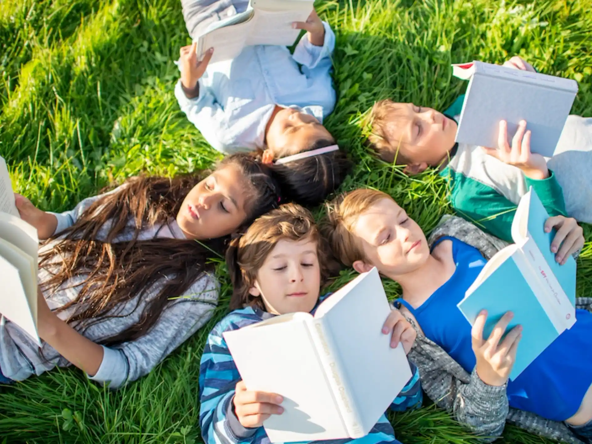 a group of children lying on the grass with a laptop