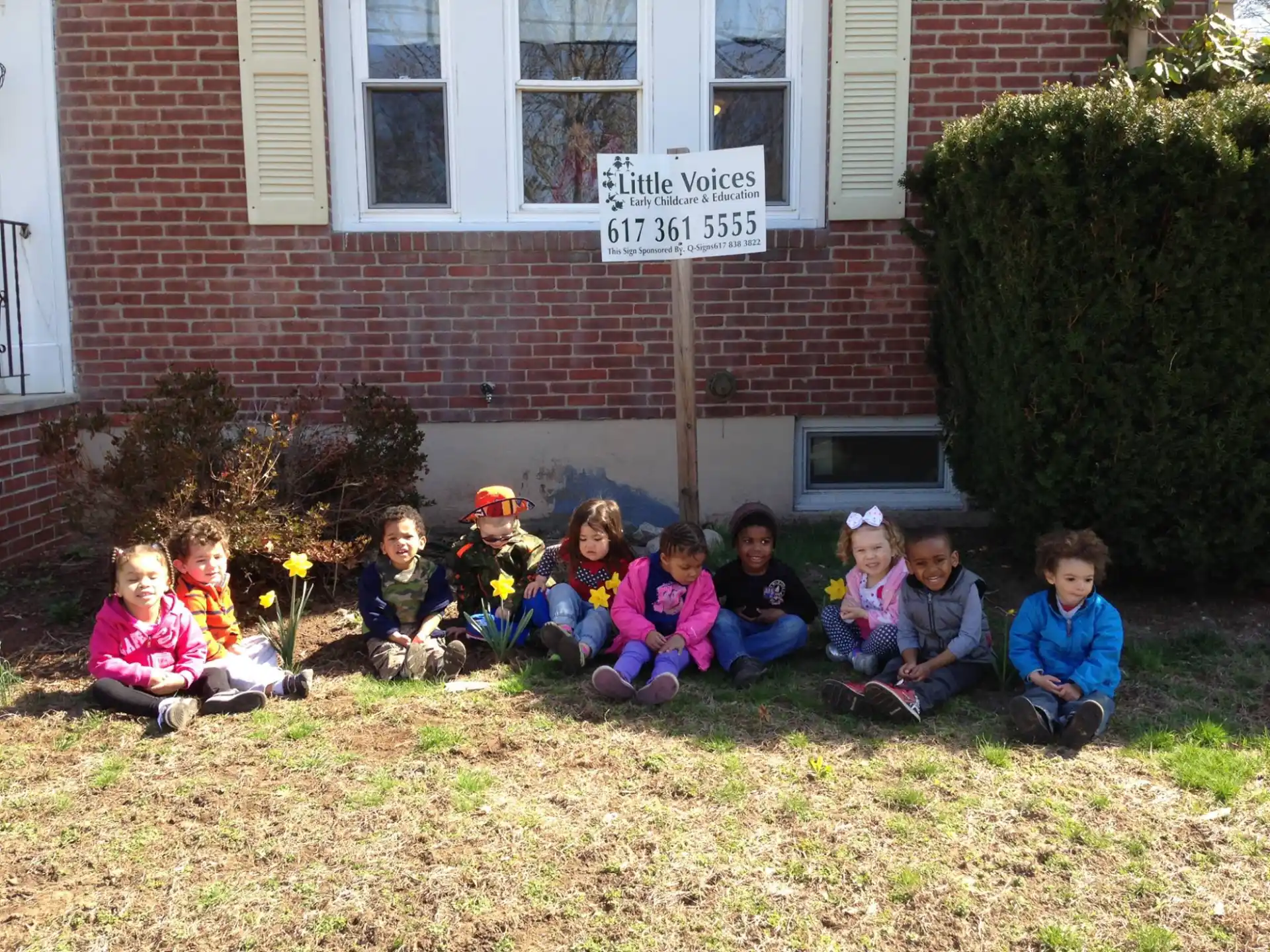 a group of children sitting on the grass in front of a brick building